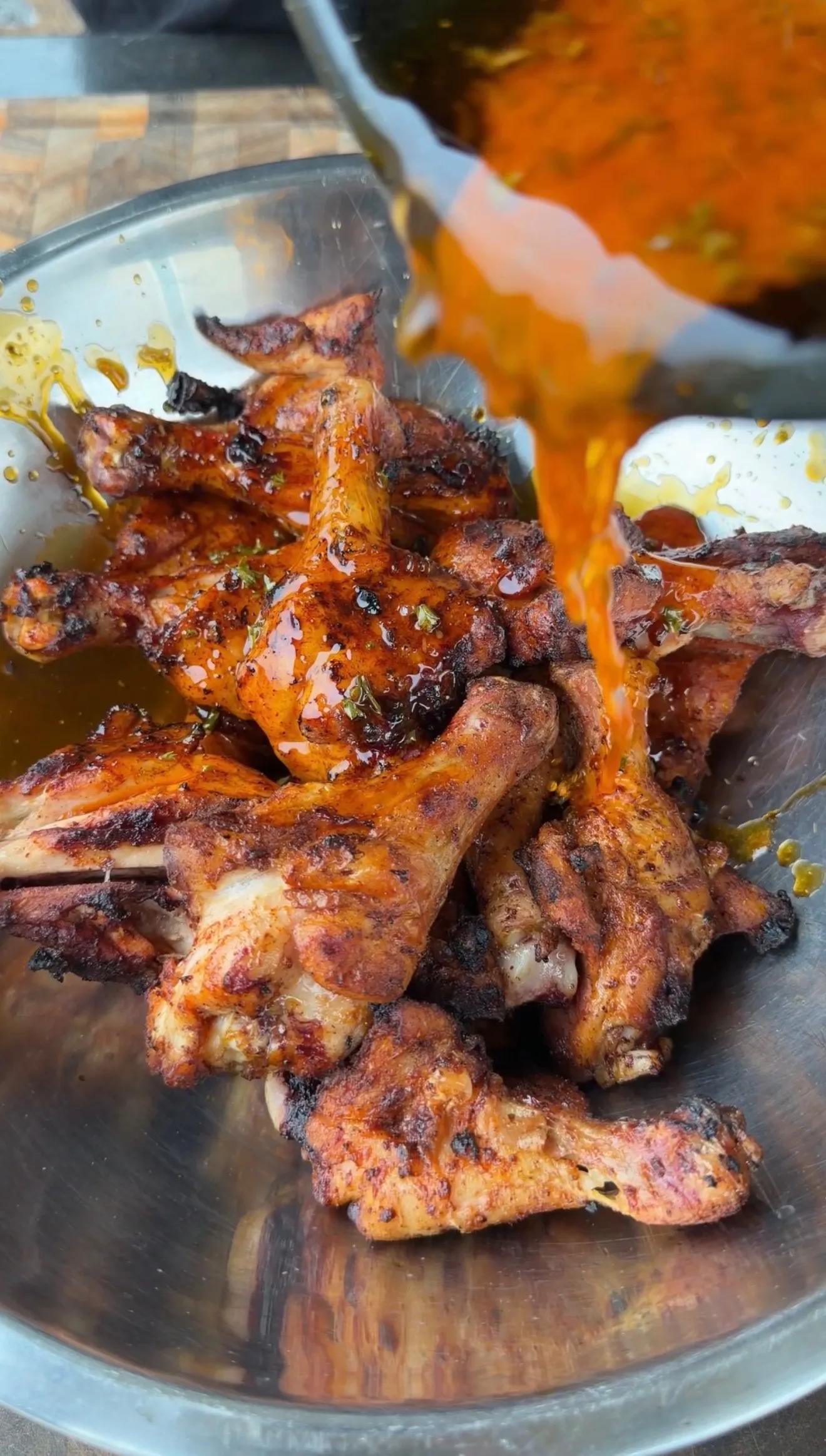 Spicy butter chili lime sauce being poured over smoky grilled chicken drumsticks in a stainless steel bowl