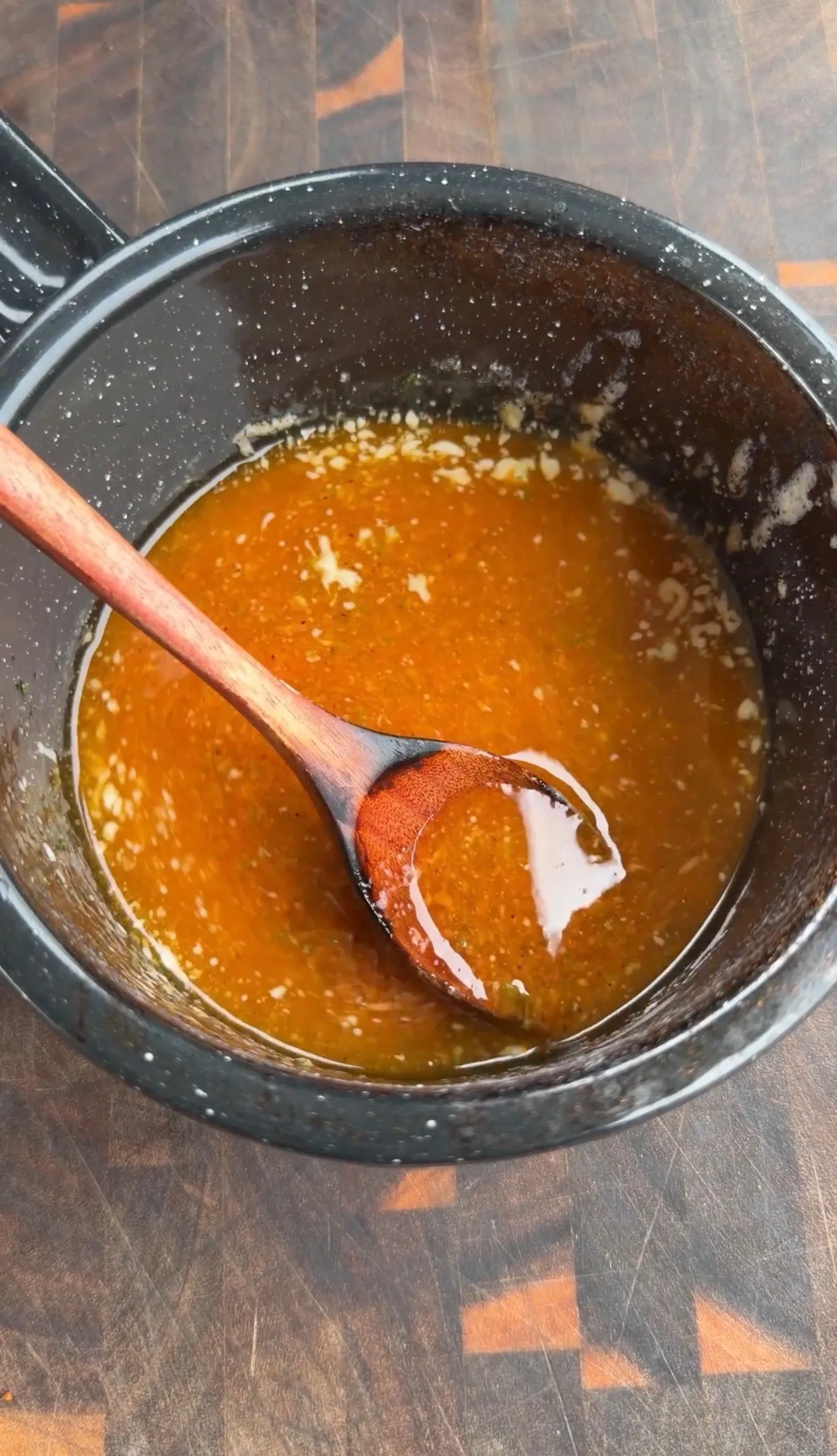 Glossy butter chili lime sauce simmering in a dark saucepan, stirred with a wooden spoon on a cutting board