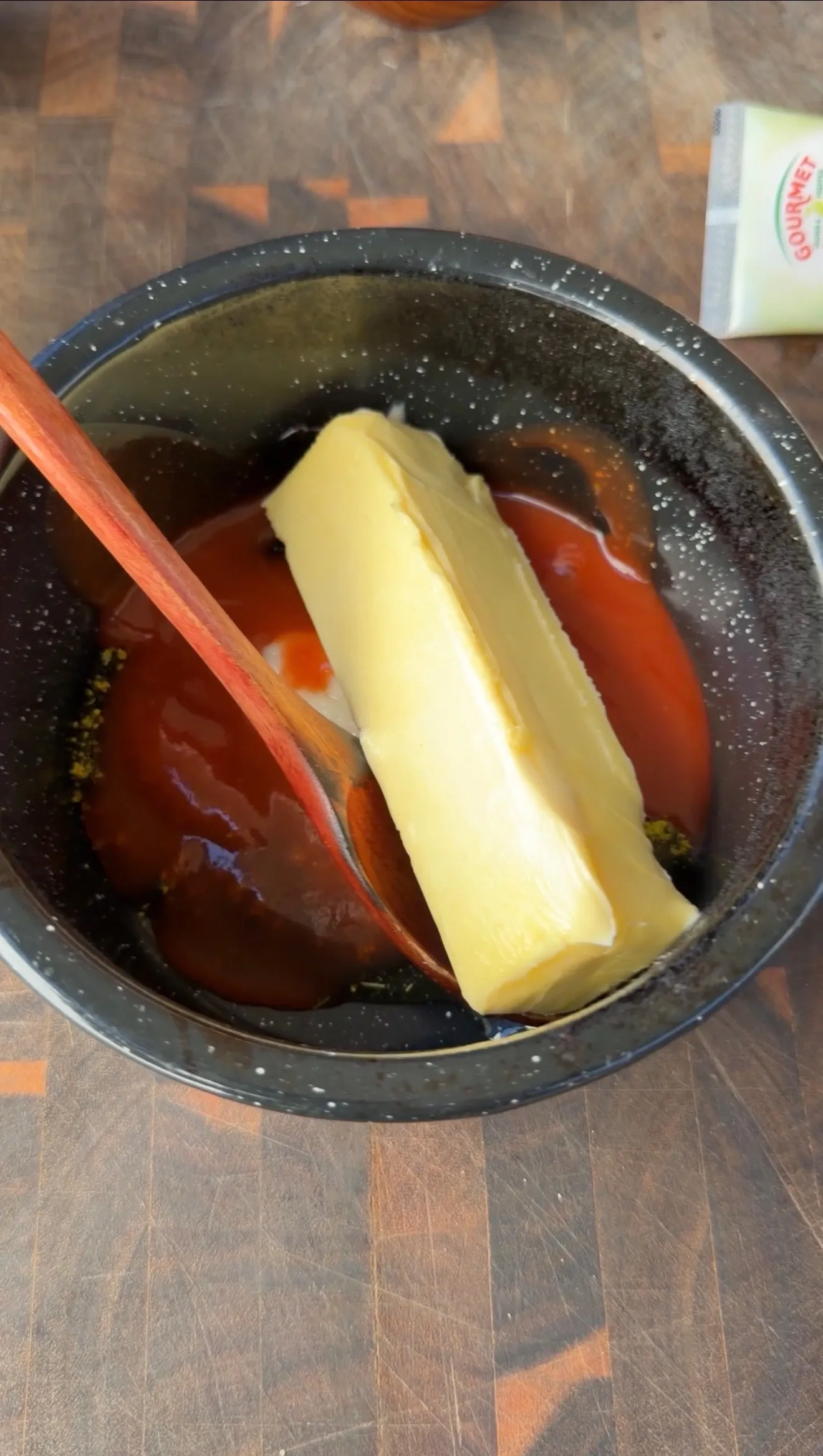 A stick of butter and hot sauce in a dark mixing bowl with a wooden spoon for Cajun lemon pepper honey chicken sauce