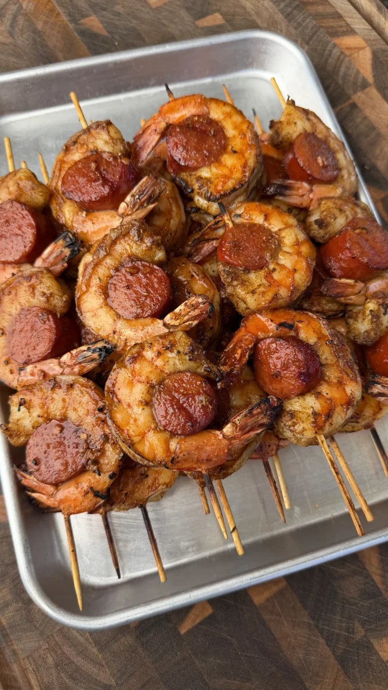 Grilled Cajun honey sausage and shrimp skewers with caramelized edges on wooden skewers in metal tray