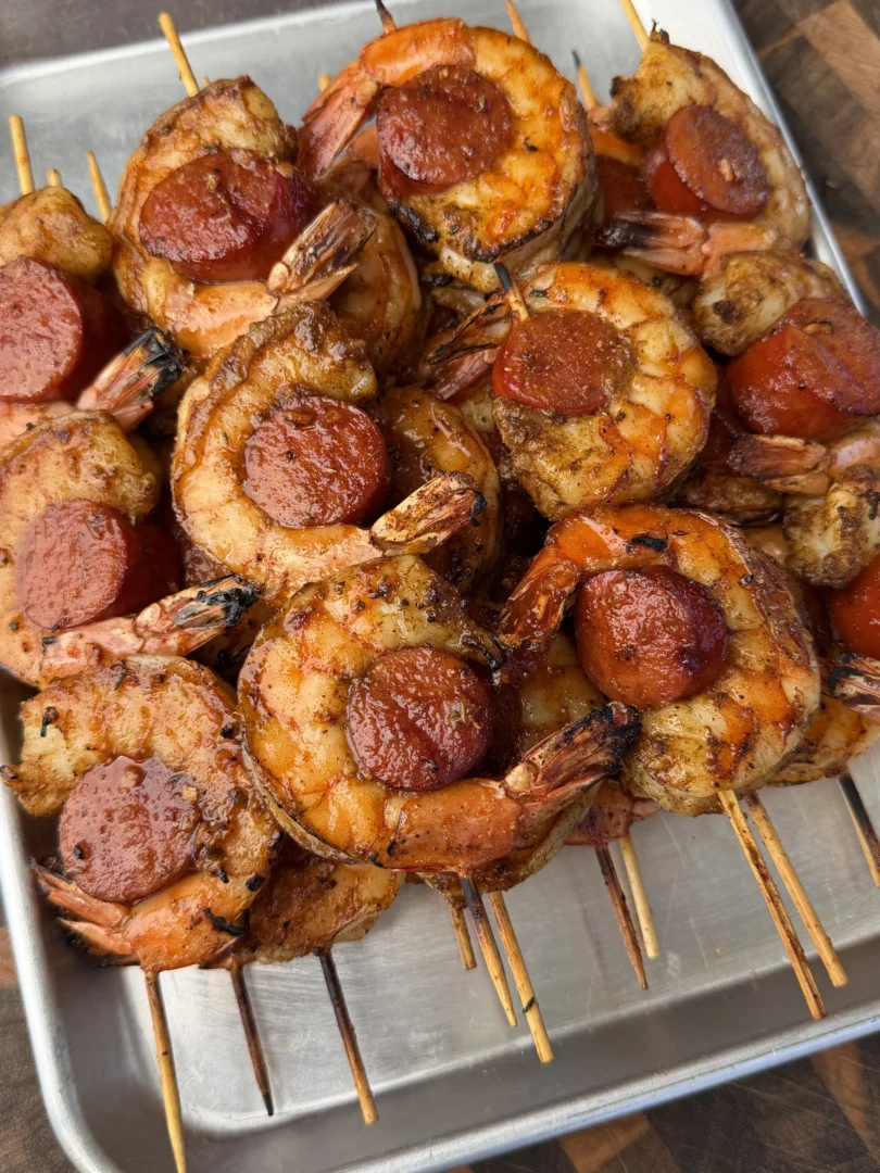 Grilled Cajun honey sausage and shrimp skewers with caramelized edges on wooden skewers in metal tray