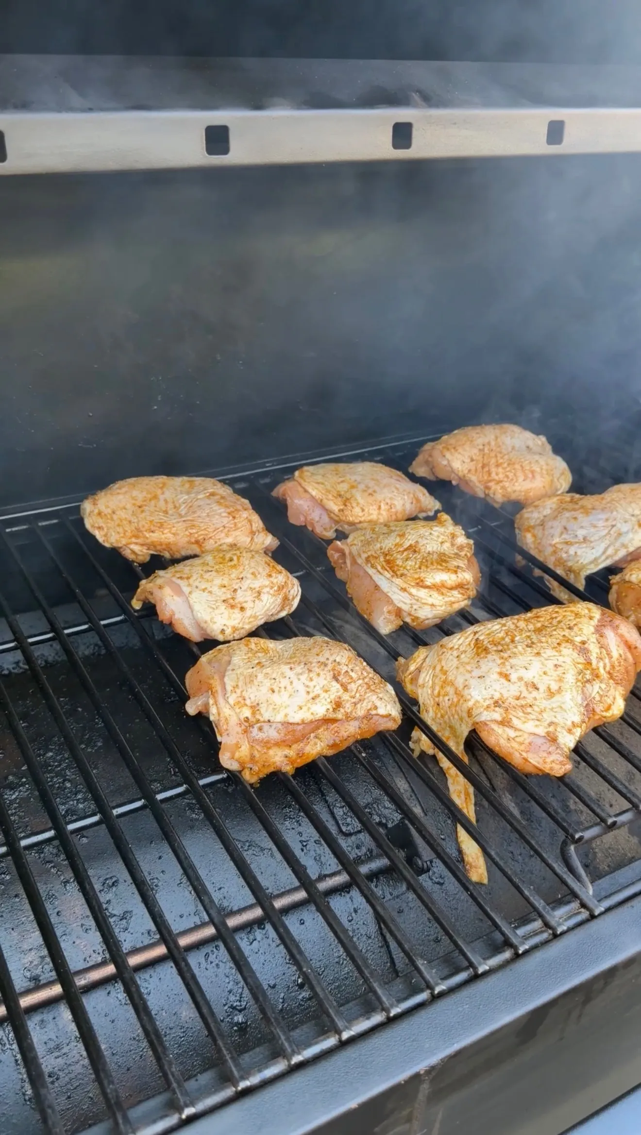Seasoned Cajun lemon pepper chicken thighs smoking on a pellet grill grate with visible smoke
