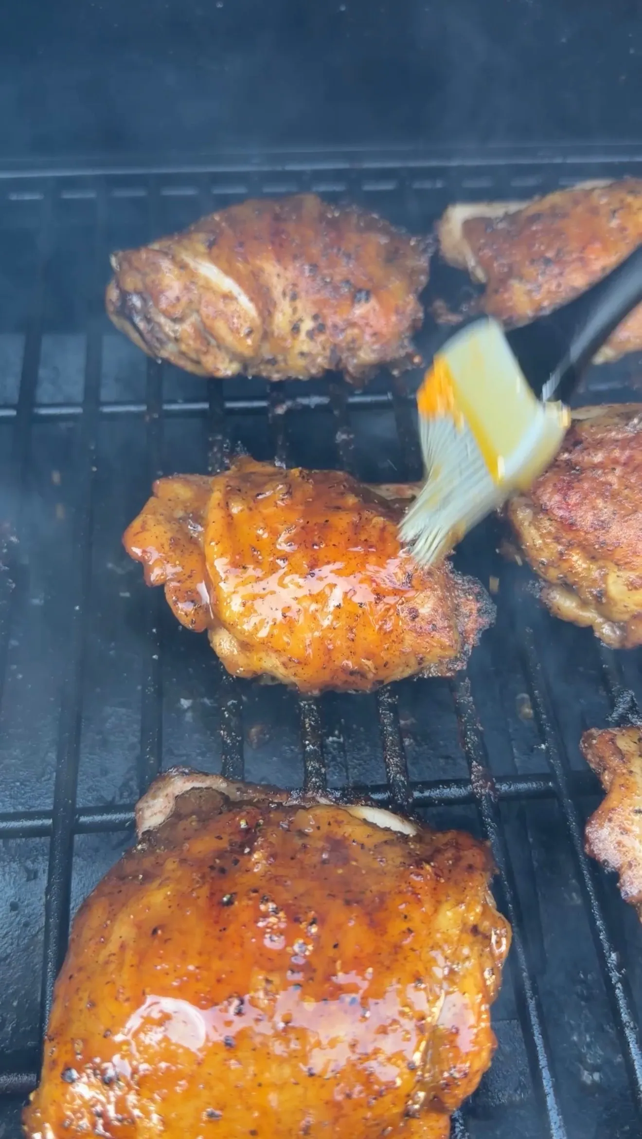 Cajun lemon pepper honey chicken thighs being basted with glaze on a smoky grill