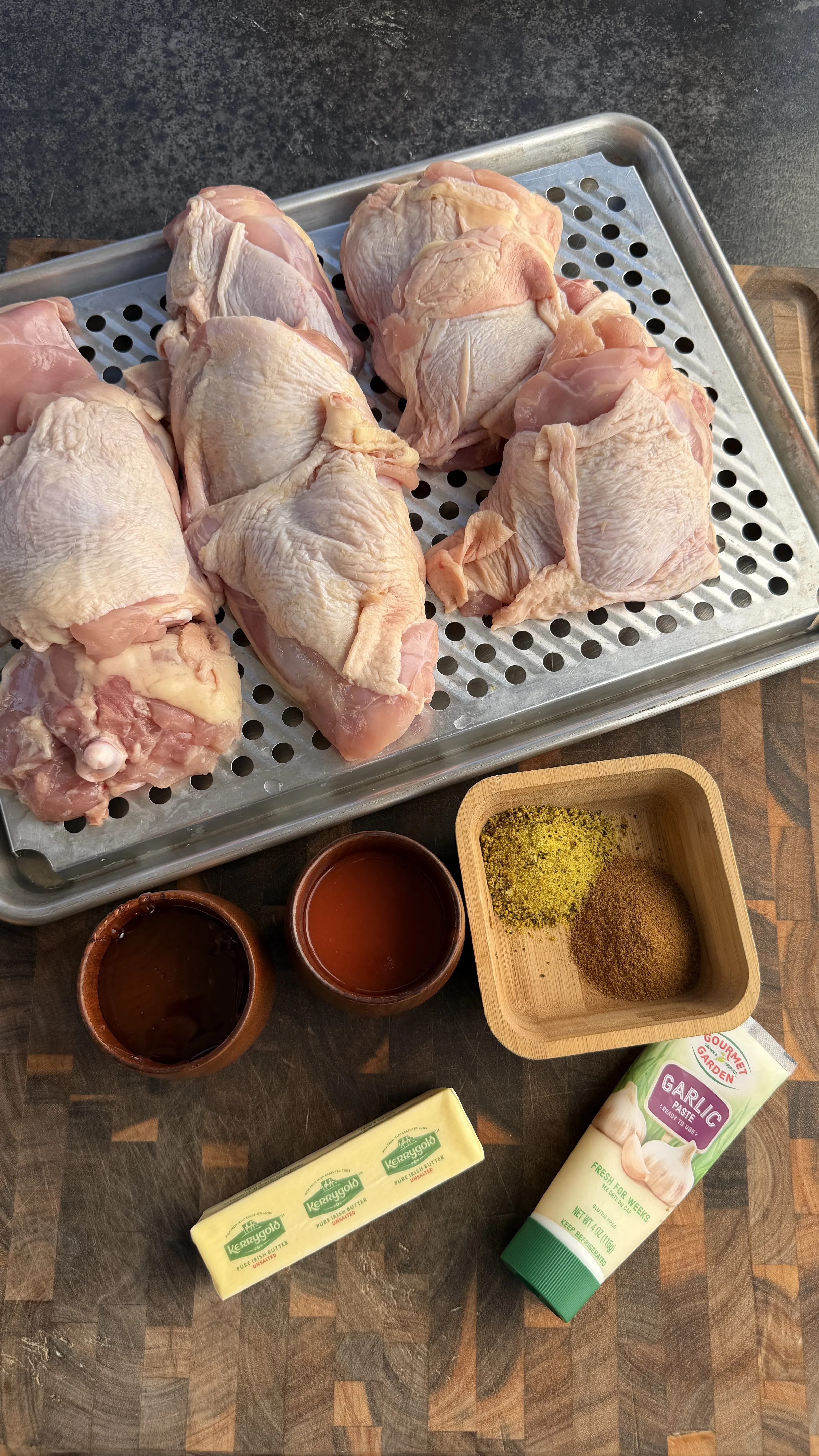 Raw bone-in chicken thighs on a baking rack with Kerrygold butter, garlic paste, spices, and sauces for Cajun Lemon Pepper Honey Chicken
