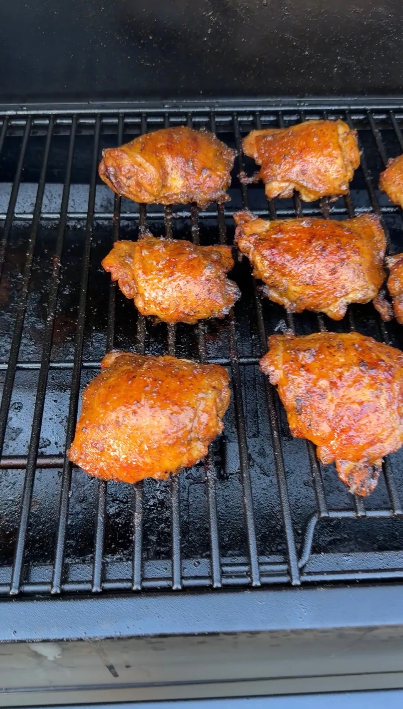 Glazed Cajun lemon pepper honey chicken thighs smoking on grill grates with caramelized orange crust