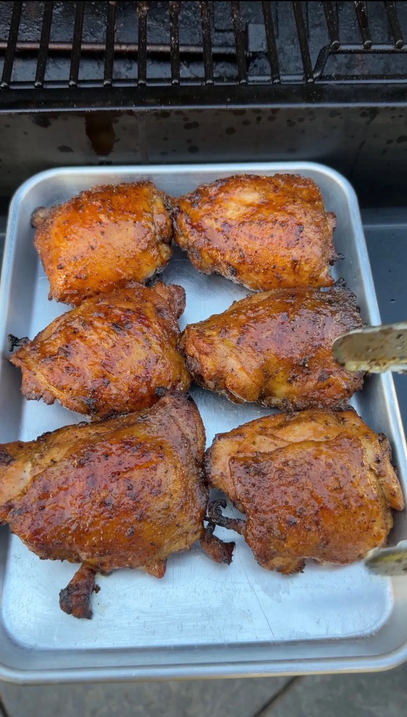 Six glazed Cajun lemon pepper honey chicken thighs on a silver tray next to a smoker grill