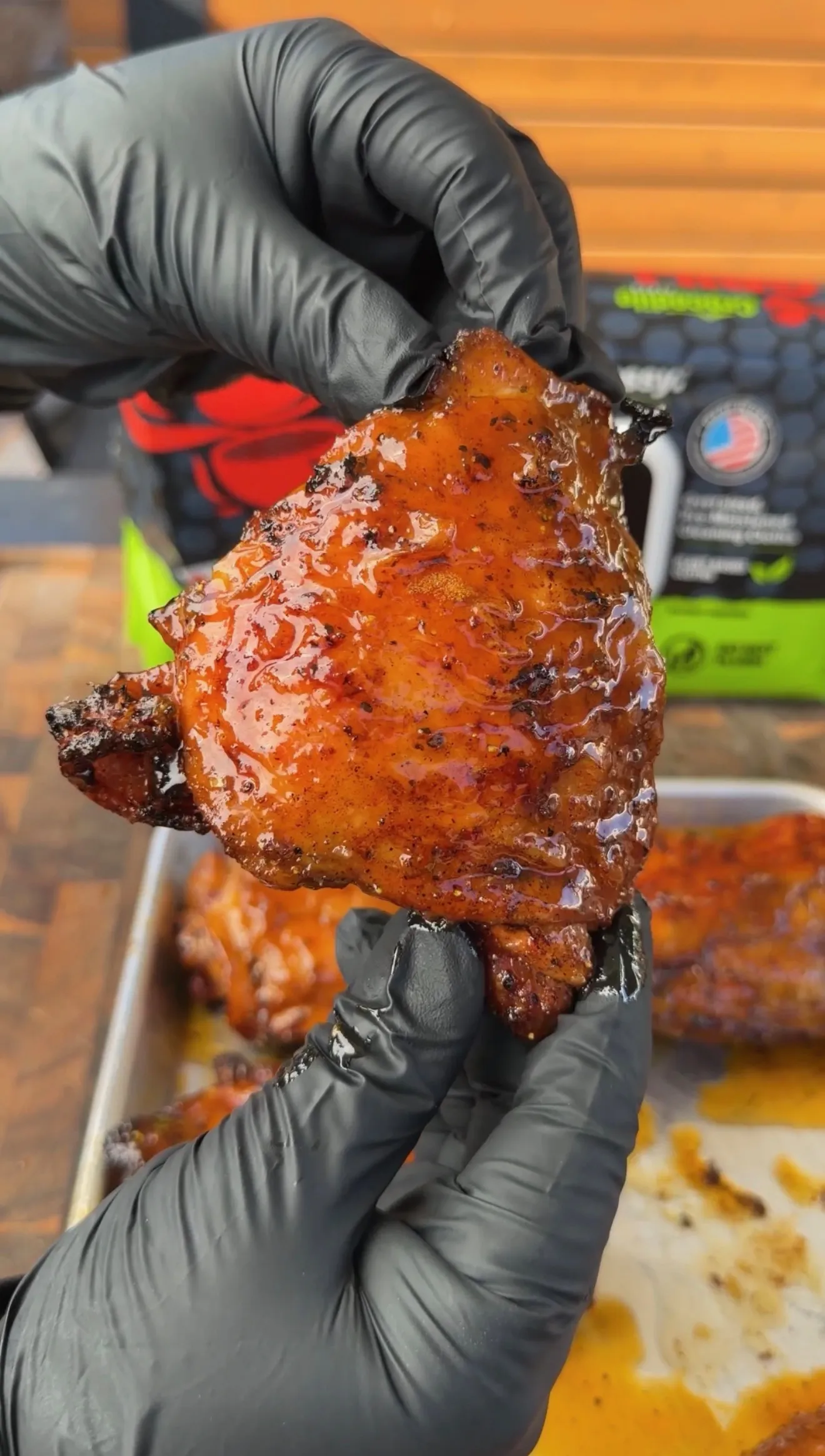 Glossy Cajun lemon pepper honey glazed chicken thigh held with black gloves, showing caramelized BBQ sauce coating