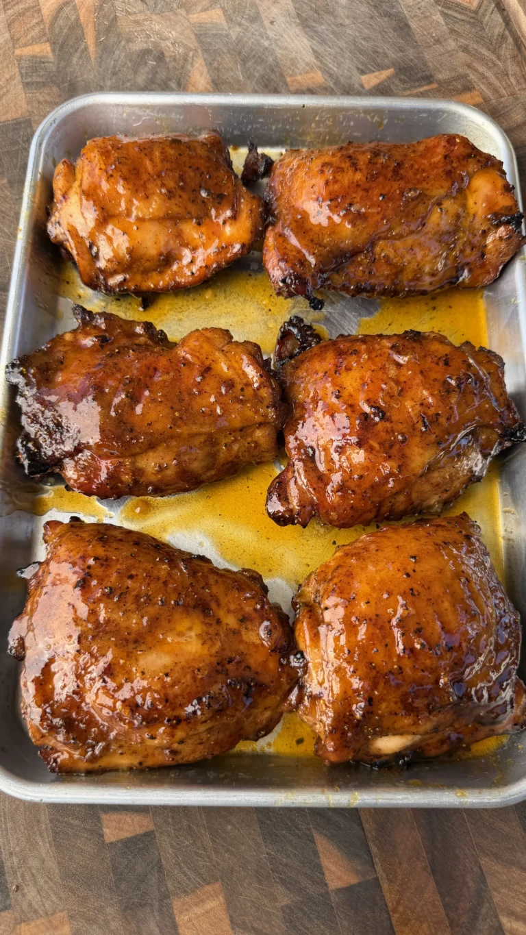 Six glossy Cajun lemon pepper honey glazed chicken thighs in a silver baking pan with golden pan juices