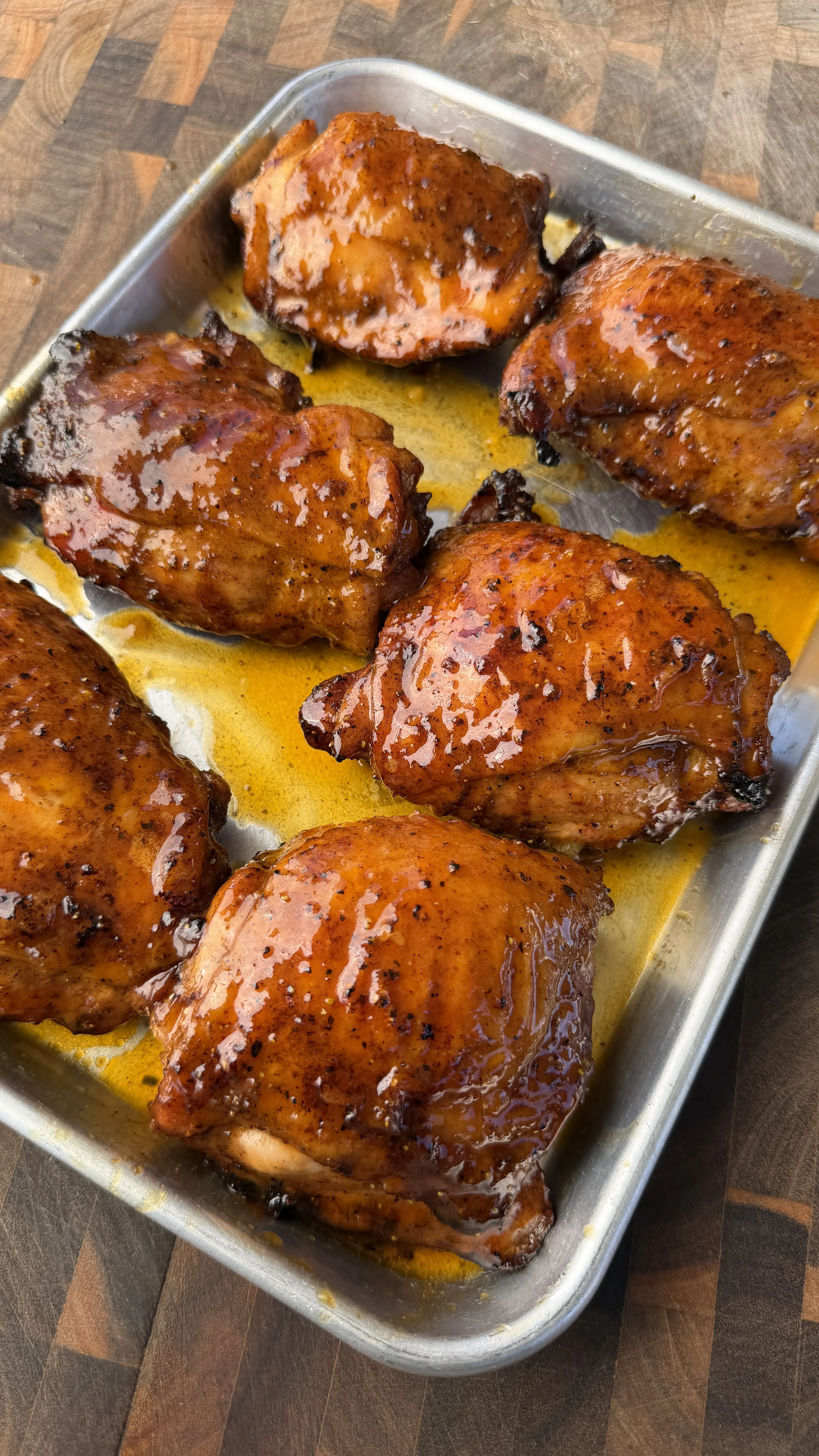 Glazed Cajun lemon pepper honey chicken thighs on a silver baking pan with golden pan juices