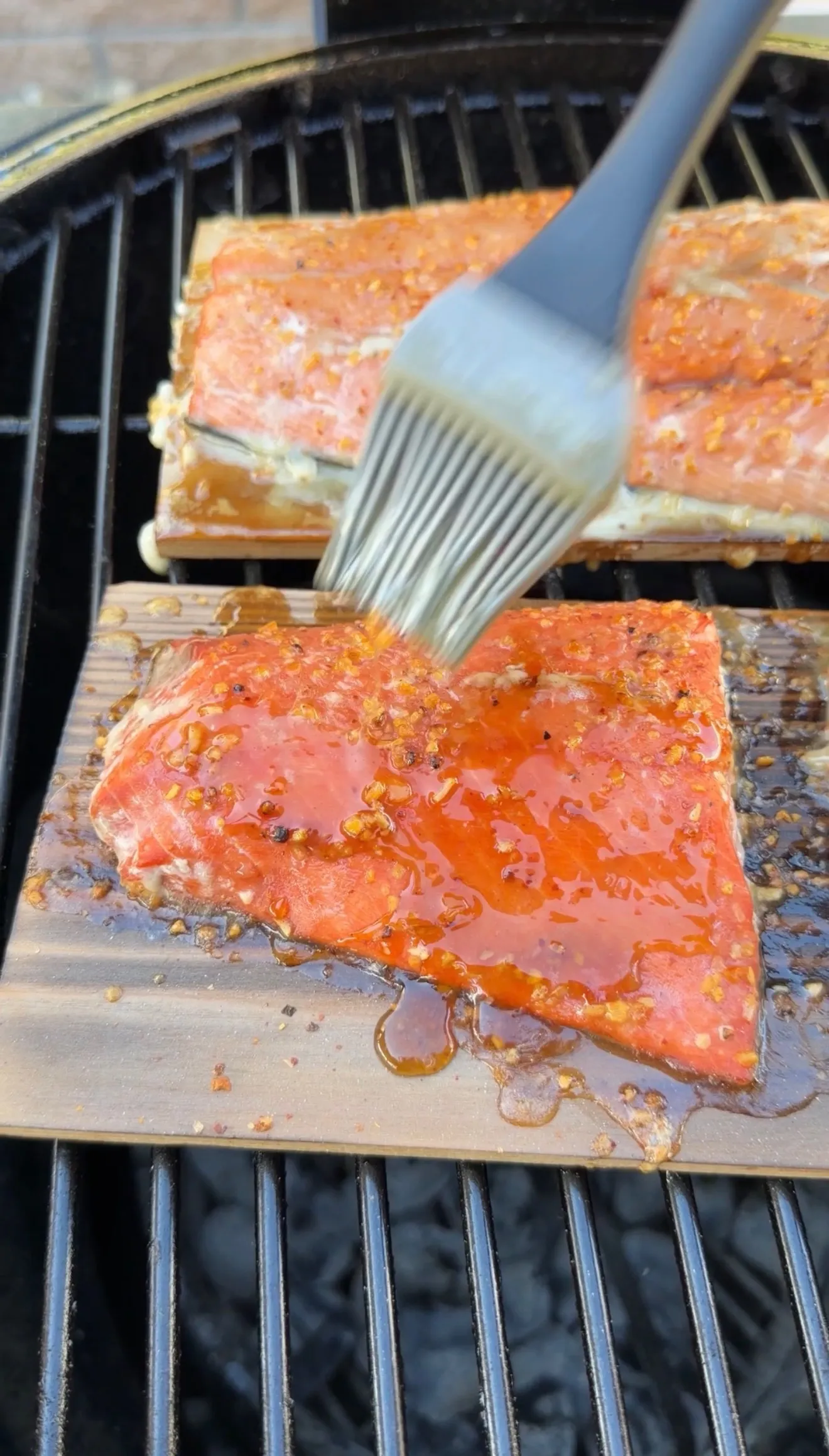 Maple bourbon glaze being brushed onto cedar plank salmon fillets cooking on an outdoor grill