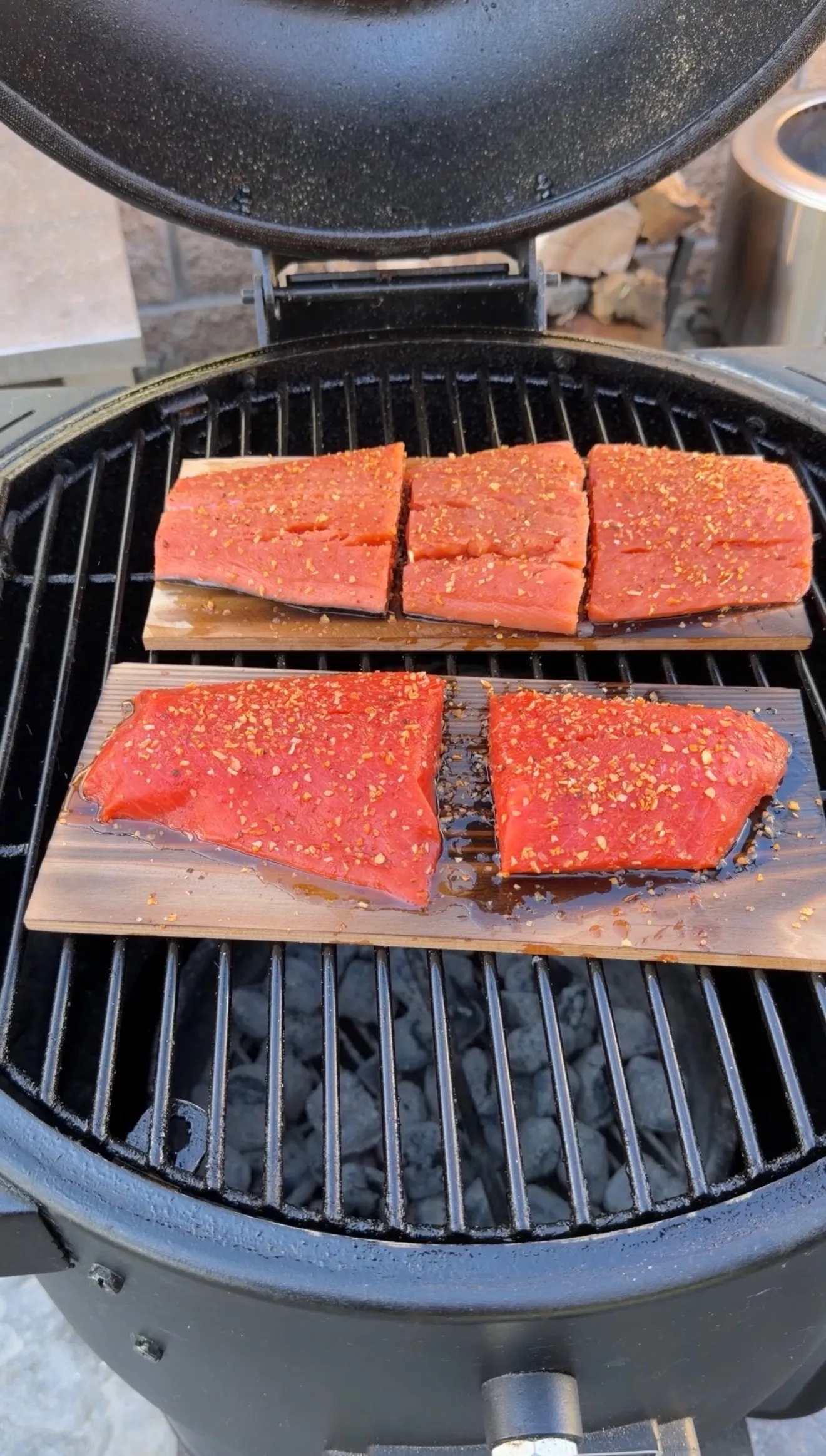Seasoned salmon fillets on cedar planks over a charcoal grill, topped with sweet BBQ rub