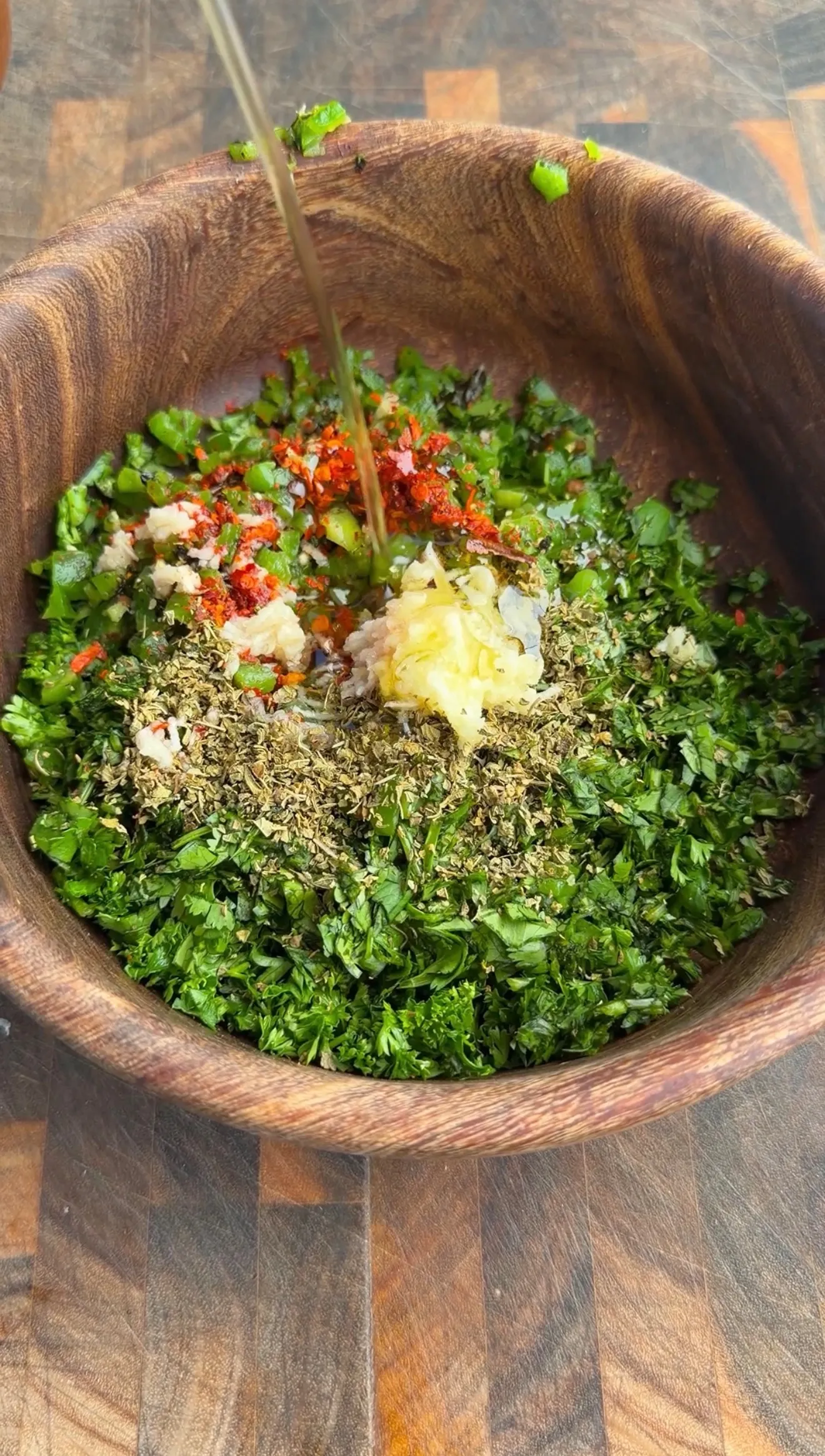 Fresh charred jalapeño chimichurri being mixed in a wooden bowl with herbs, spices, and garlic