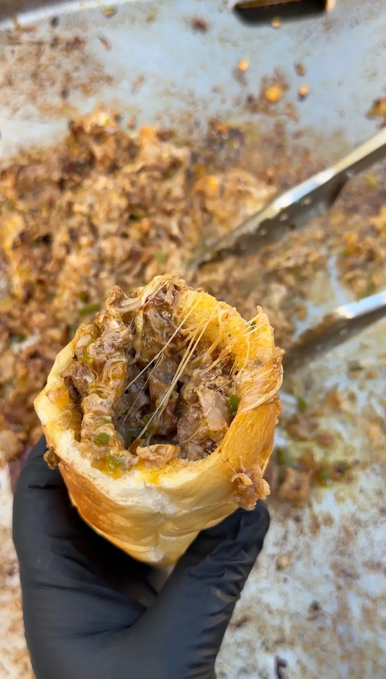 Hand holding a cheesesteak stuffed bolillo bread roll cut open, revealing melted cheese, steak, peppers, and onions