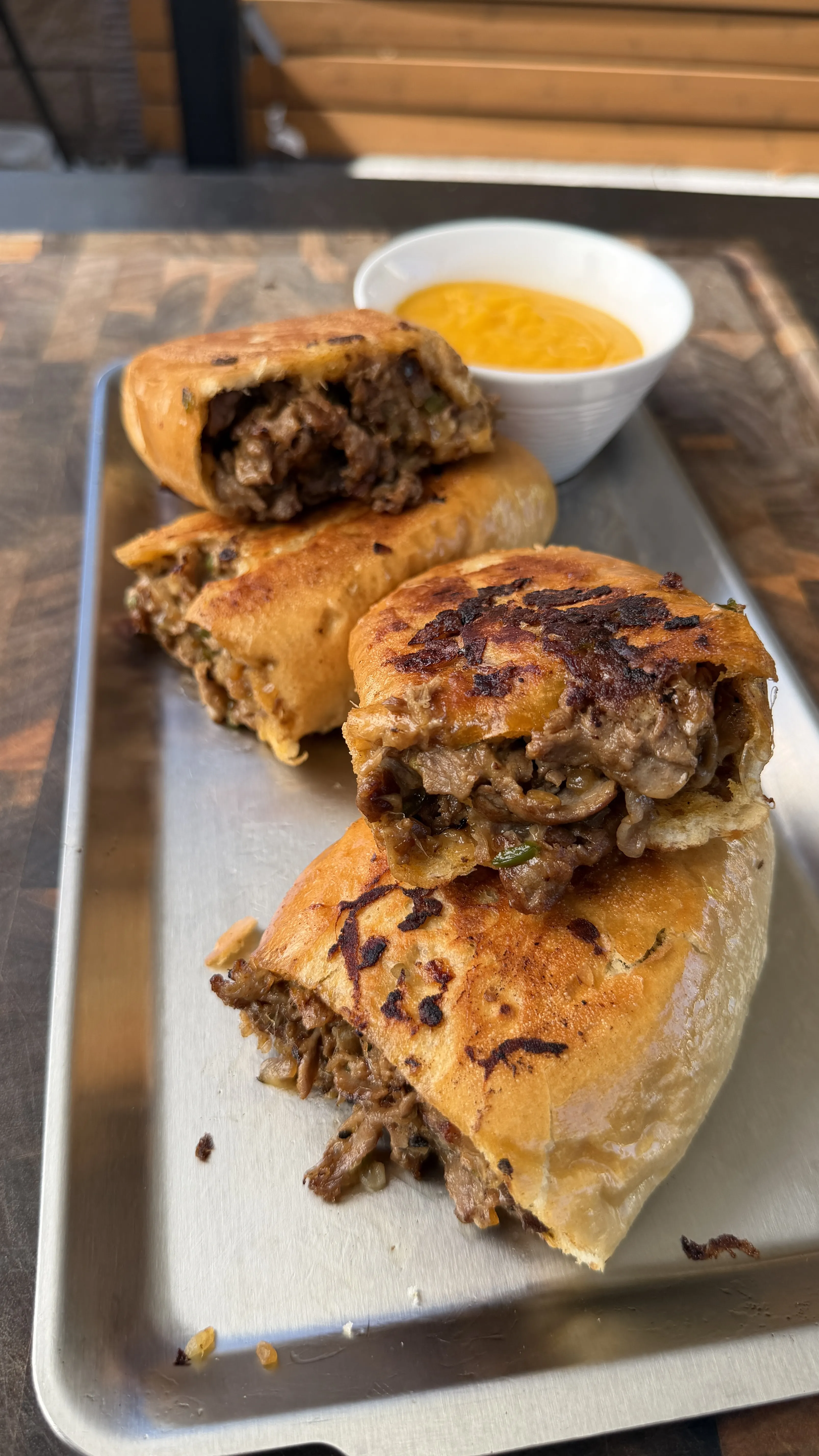 Sliced cheesesteak stuffed bolillo bread on a metal tray with melted cheese filling and a side of queso dipping sauce