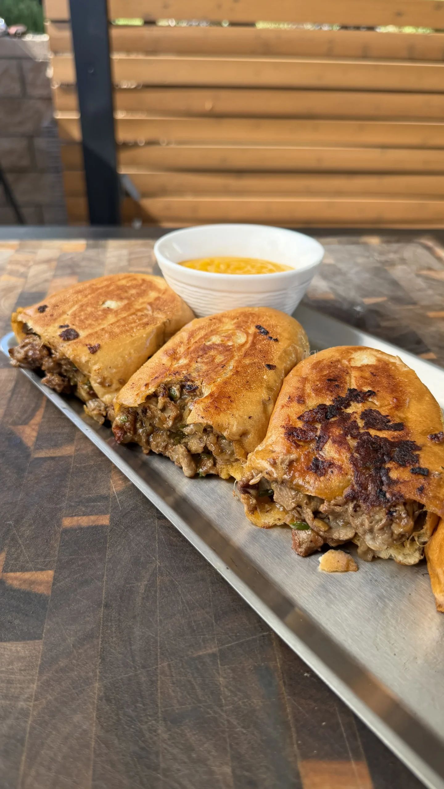 Sliced cheesesteak stuffed bolillo bread on a metal tray with a side of cheese dipping sauce