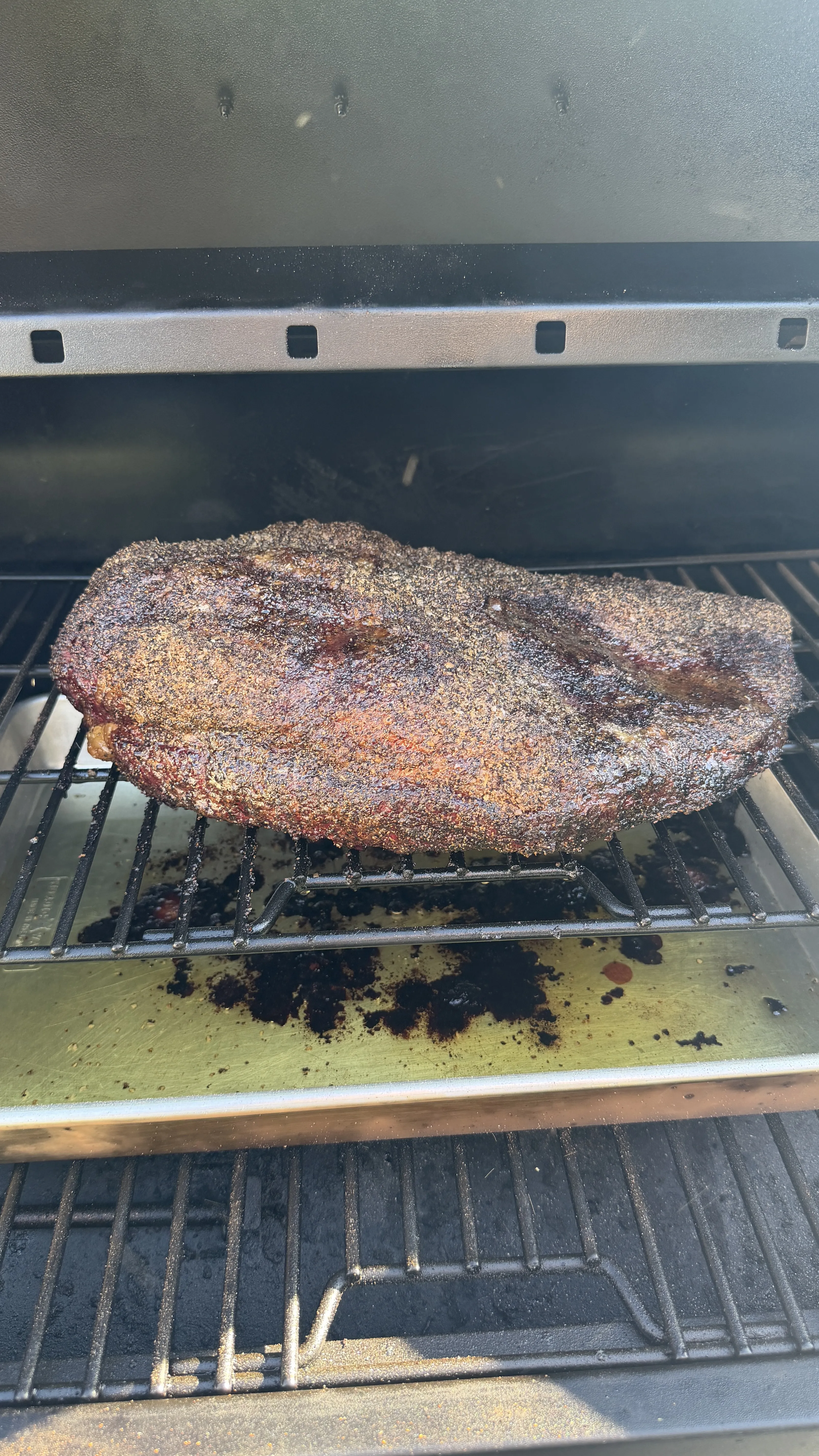 Whole beef brisket with dark spice bark crust smoking on grill grates in a pellet smoker