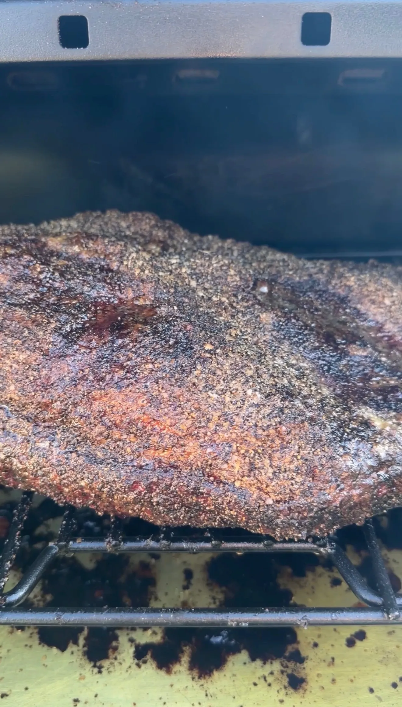 Whole beef brisket with dark spice bark crust smoking on a BBQ smoker grate