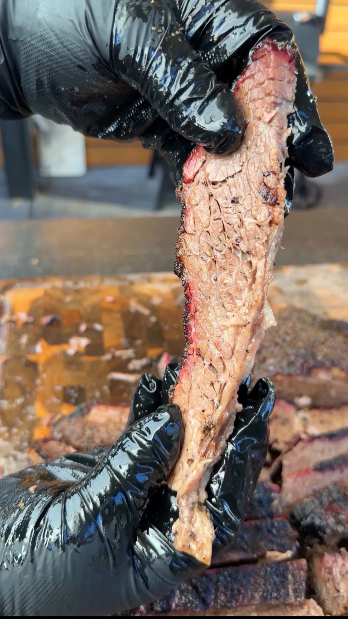 Pitmaster in black gloves holding up a tender, juicy slice of cherry smoked brisket showing smoke ring
