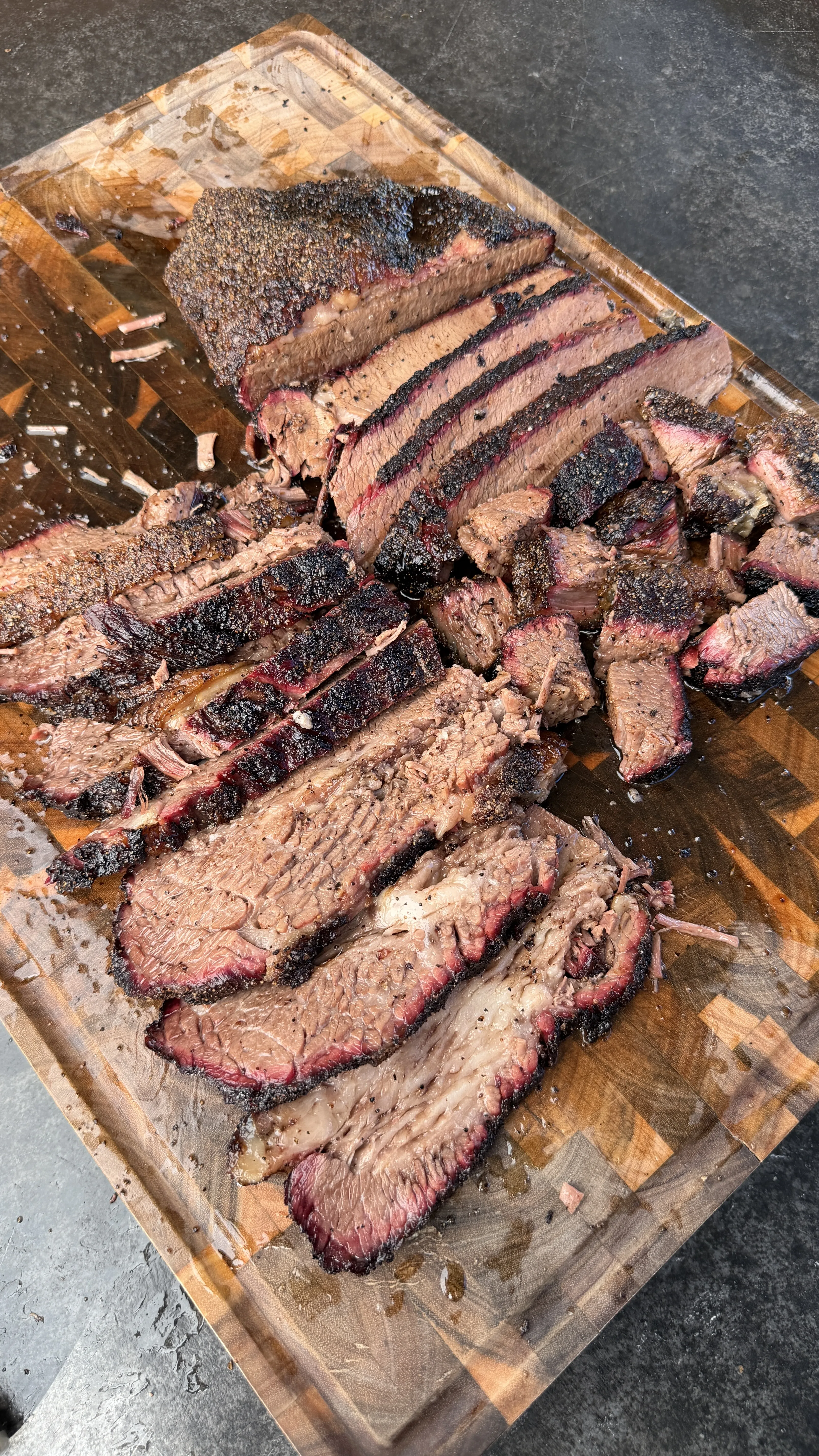 Thick slices of cherry smoked brisket with dark bark crust on a wooden cutting board