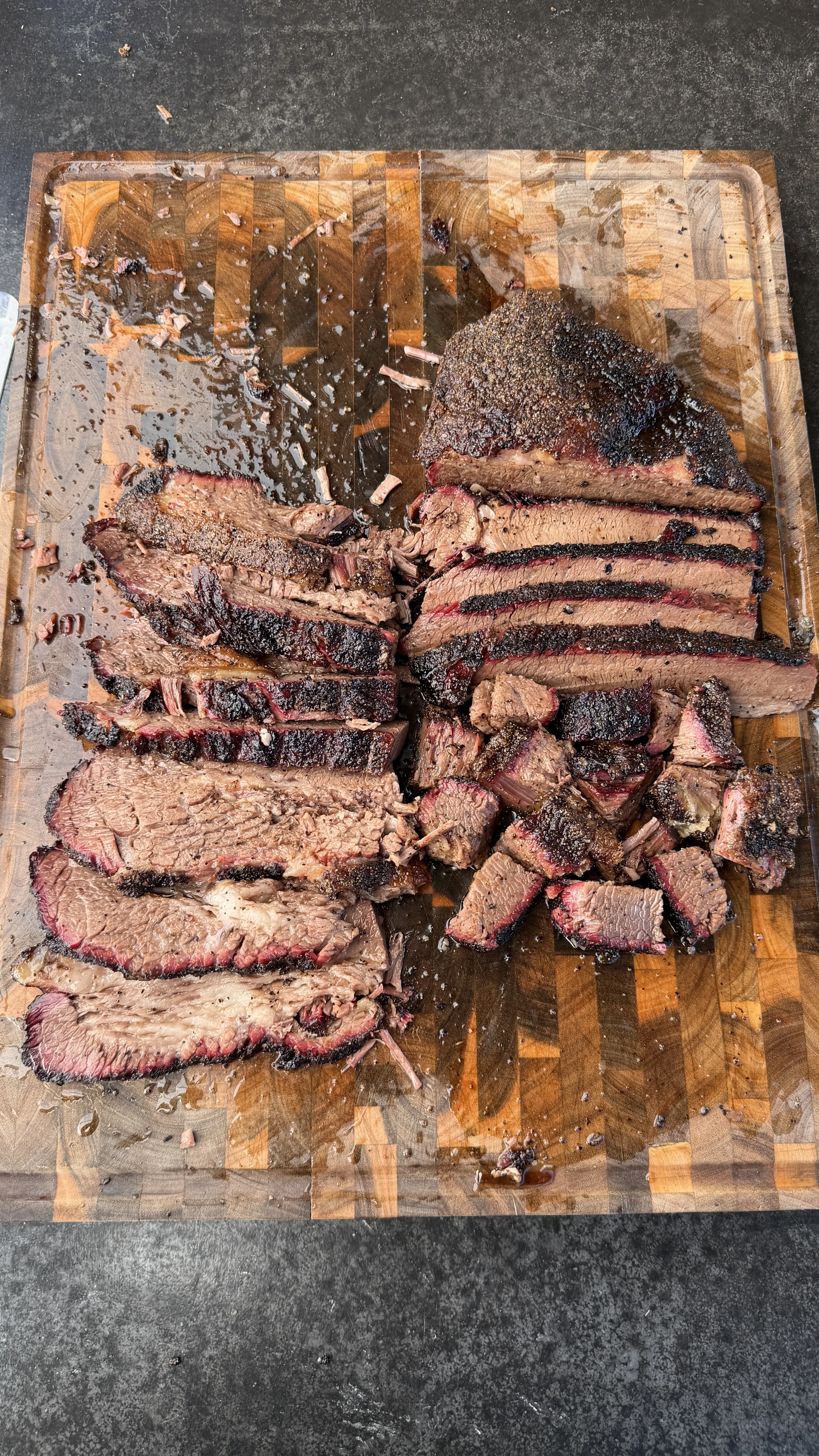 Thick slices of cherry smoked brisket with dark bark on a wooden end-grain cutting board with meat juices