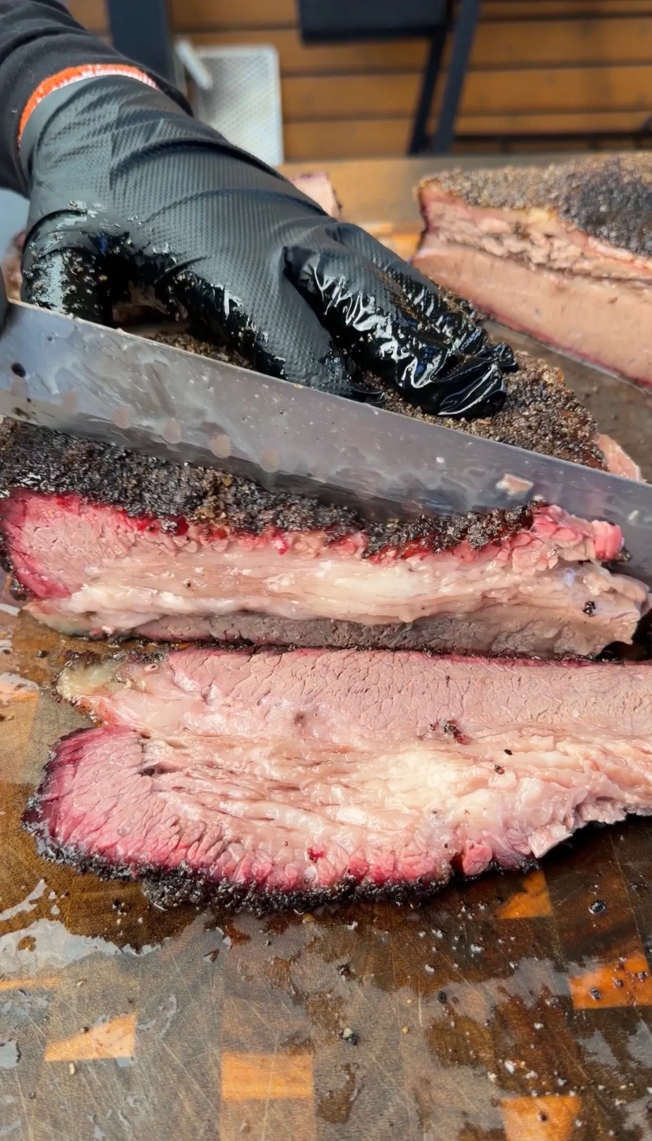 Thick slices of cherry smoked brisket with dark bark crust being cut on a wooden butcher block