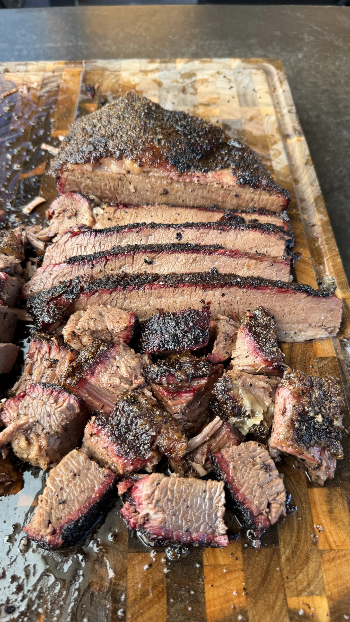 Thick slices of cherry smoked brisket with dark bark and pink smoke ring on a wooden cutting board