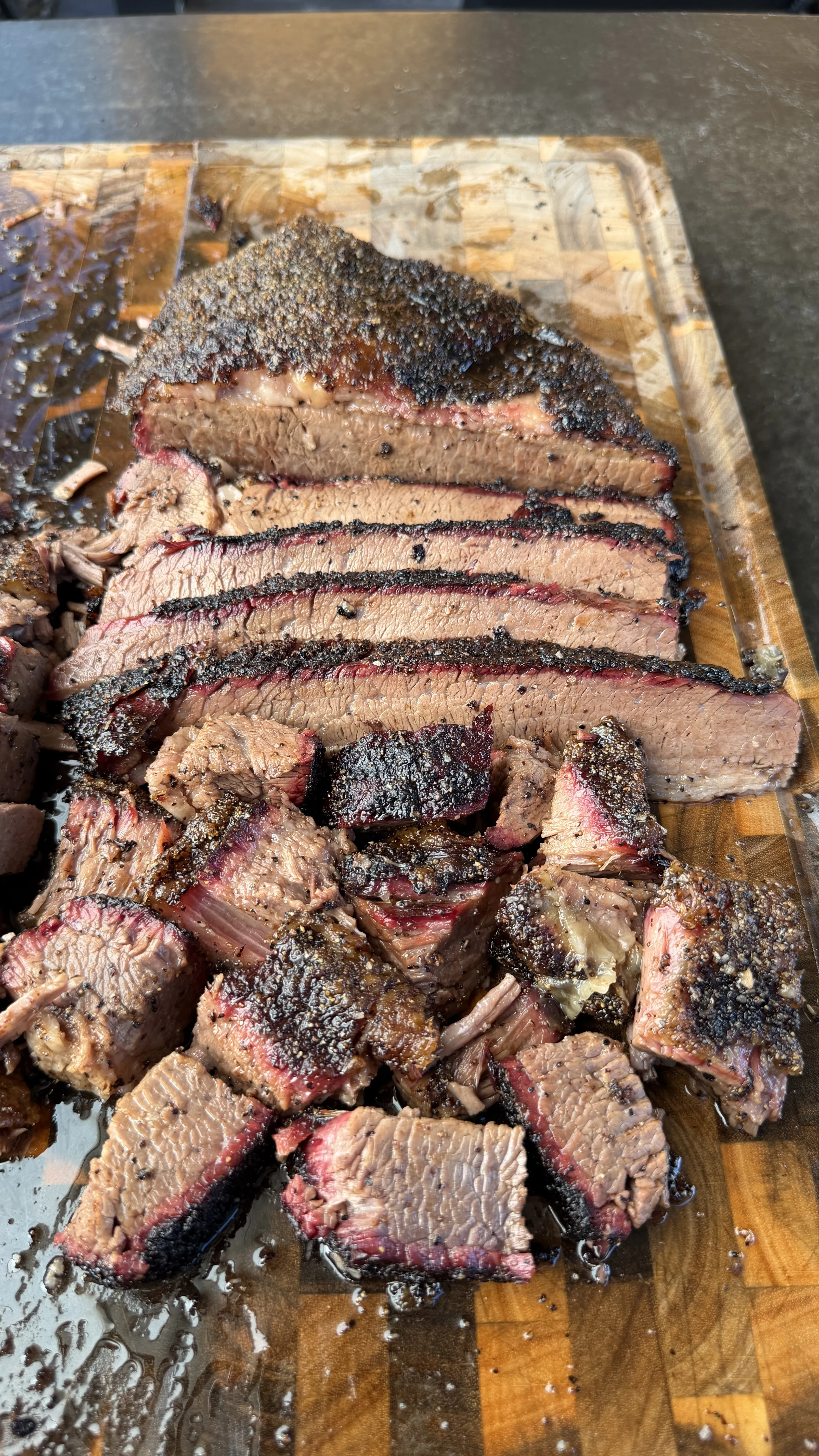 Thick slices of cherry smoked brisket with dark bark and pink smoke ring on a wooden cutting board