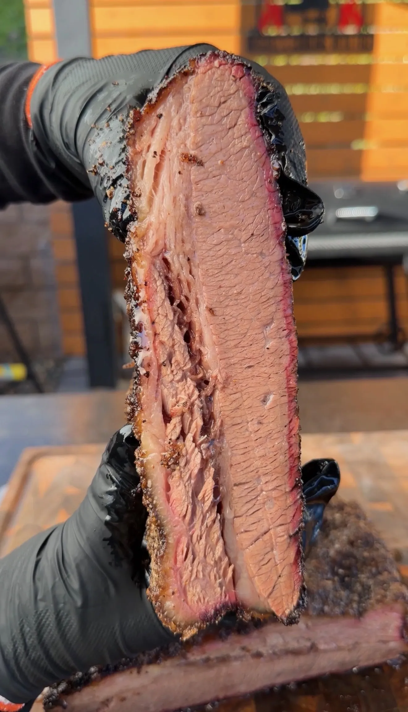 Gloved hands holding a thick slice of cherry smoked brisket showing a deep pink smoke ring and dark bark crust