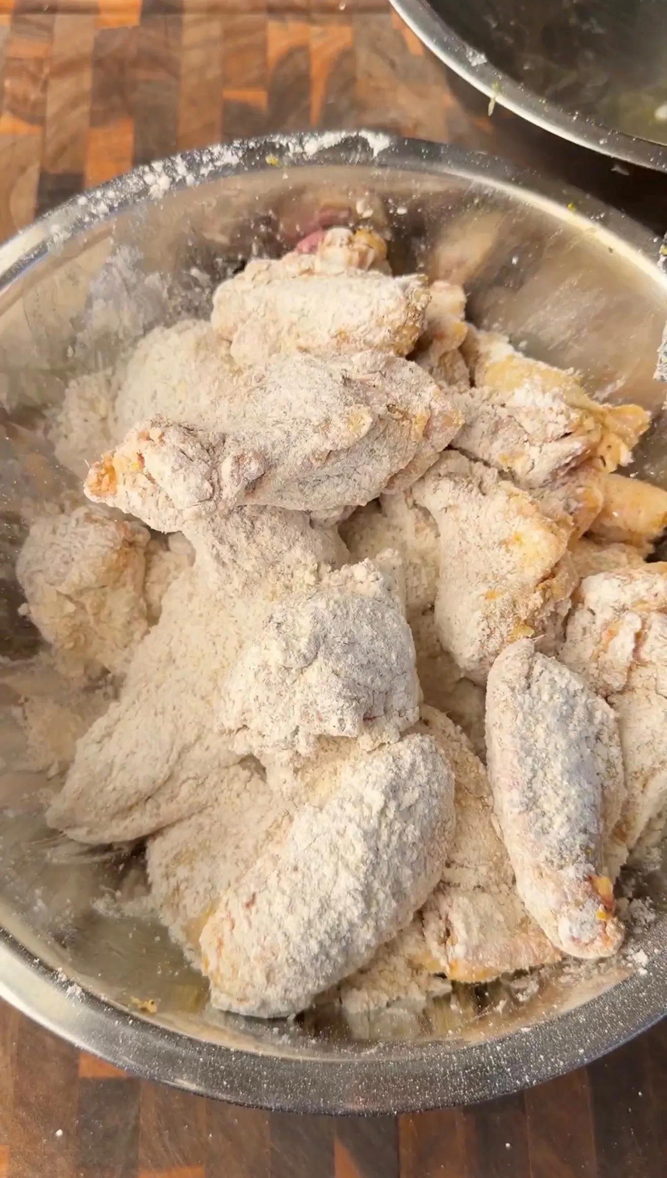 Raw chicken wings tossed in seasoned flour mixture in a stainless steel bowl, ready for frying