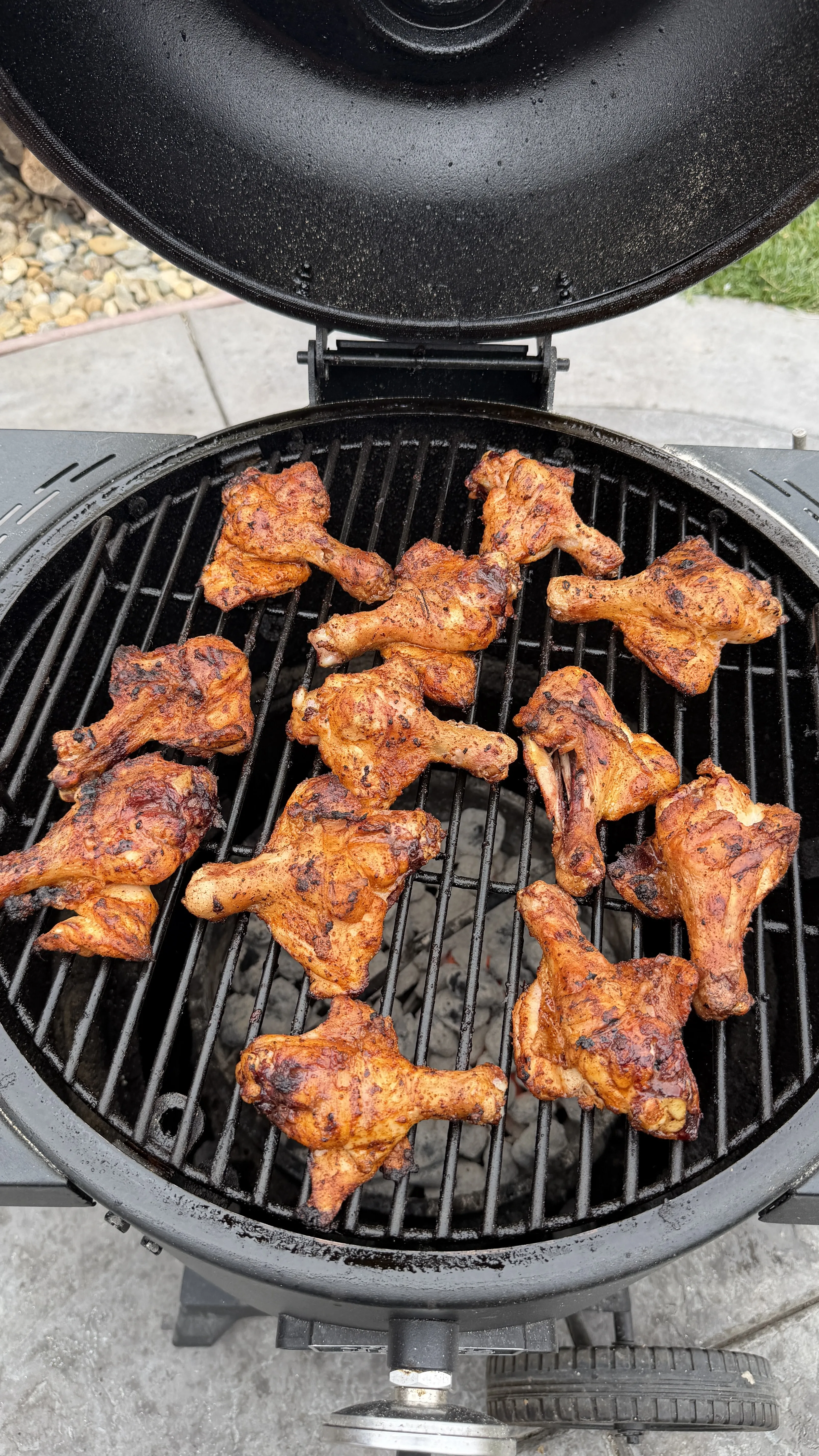 Butter chili lime grilled chicken drumsticks cooking on a round charcoal kamado grill, golden-brown with char marks