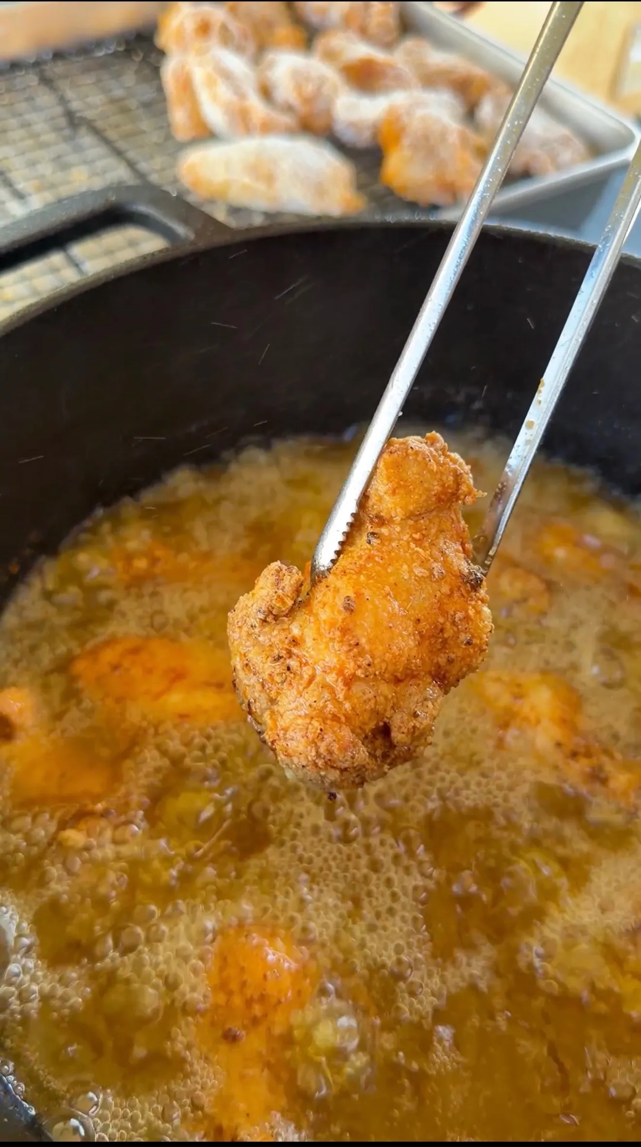 Tongs lifting a golden crispy fried honey lemon pepper wing from bubbling hot oil in a cast iron skillet