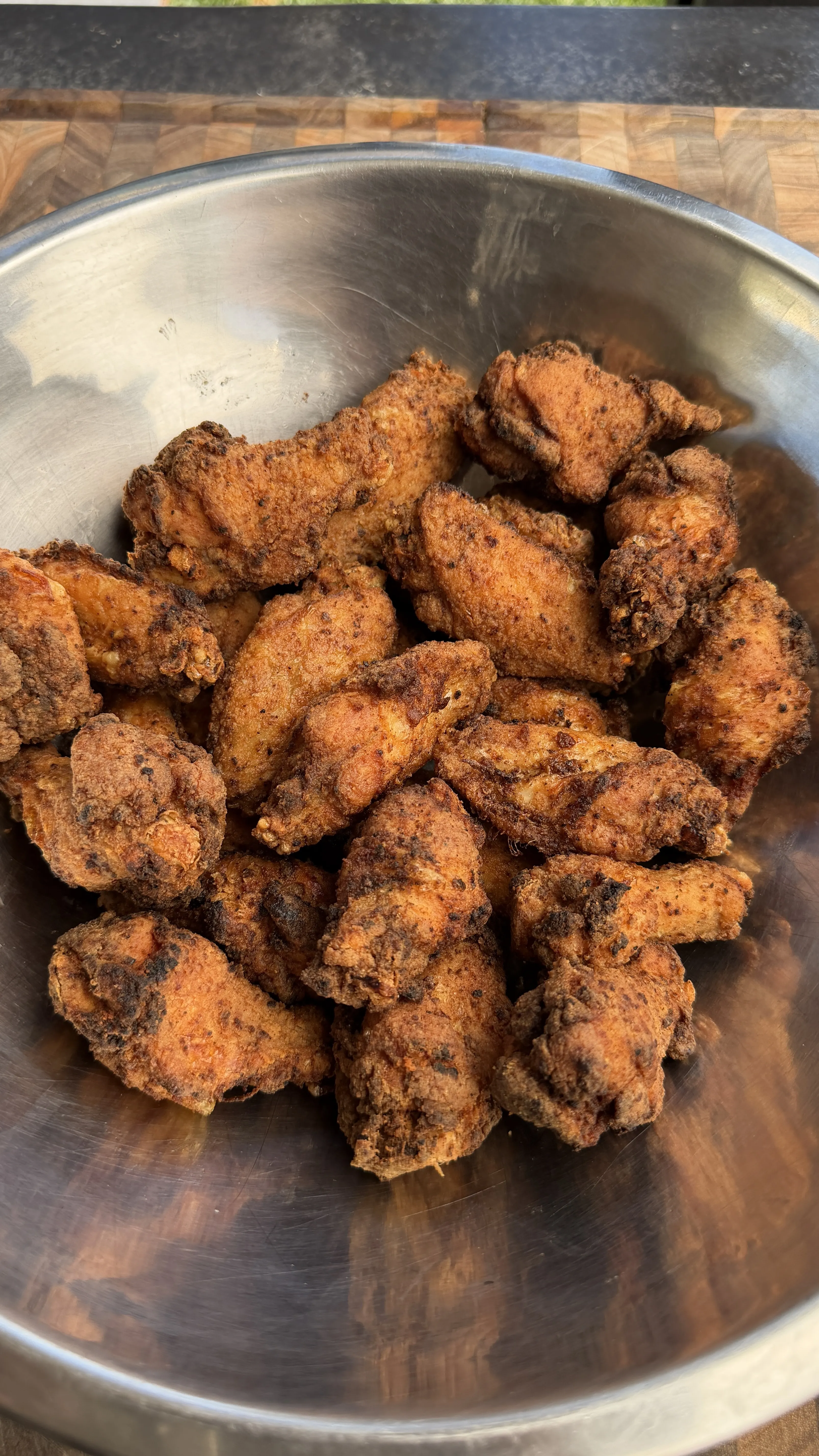 A large stainless steel bowl piled high with crispy fried honey lemon pepper chicken wings on a wooden cutting board