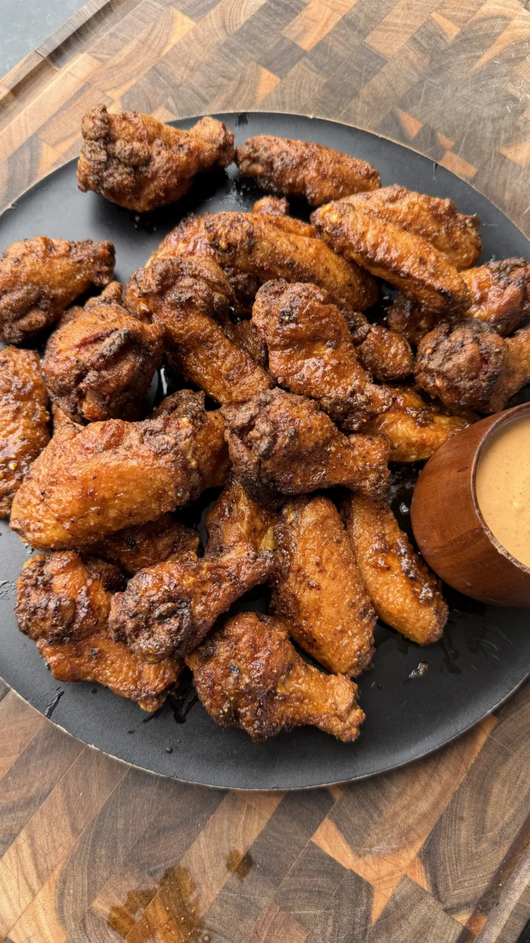Crispy fried honey lemon pepper chicken wings piled on a dark plate with a wooden dipping sauce bowl