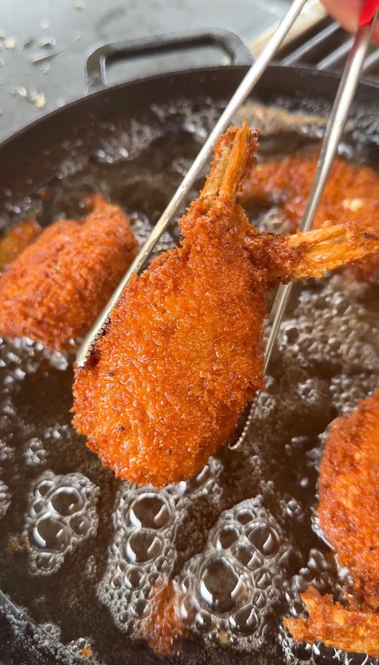 Golden-brown breaded jalapeño popper stuffed shrimp being lifted from bubbling hot oil with tongs