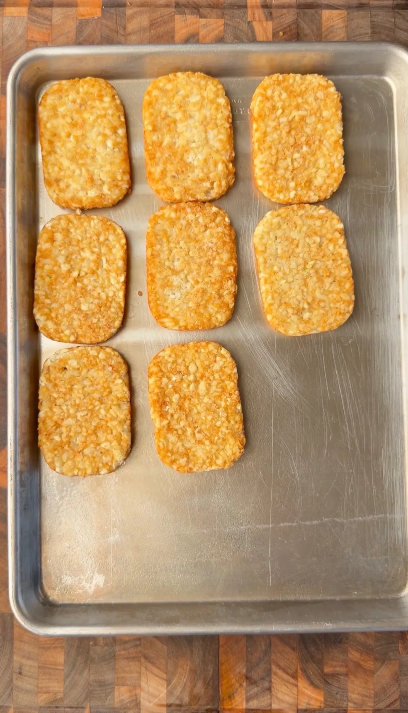 Eight golden crispy hash brown patties arranged on a metal baking sheet after cooking