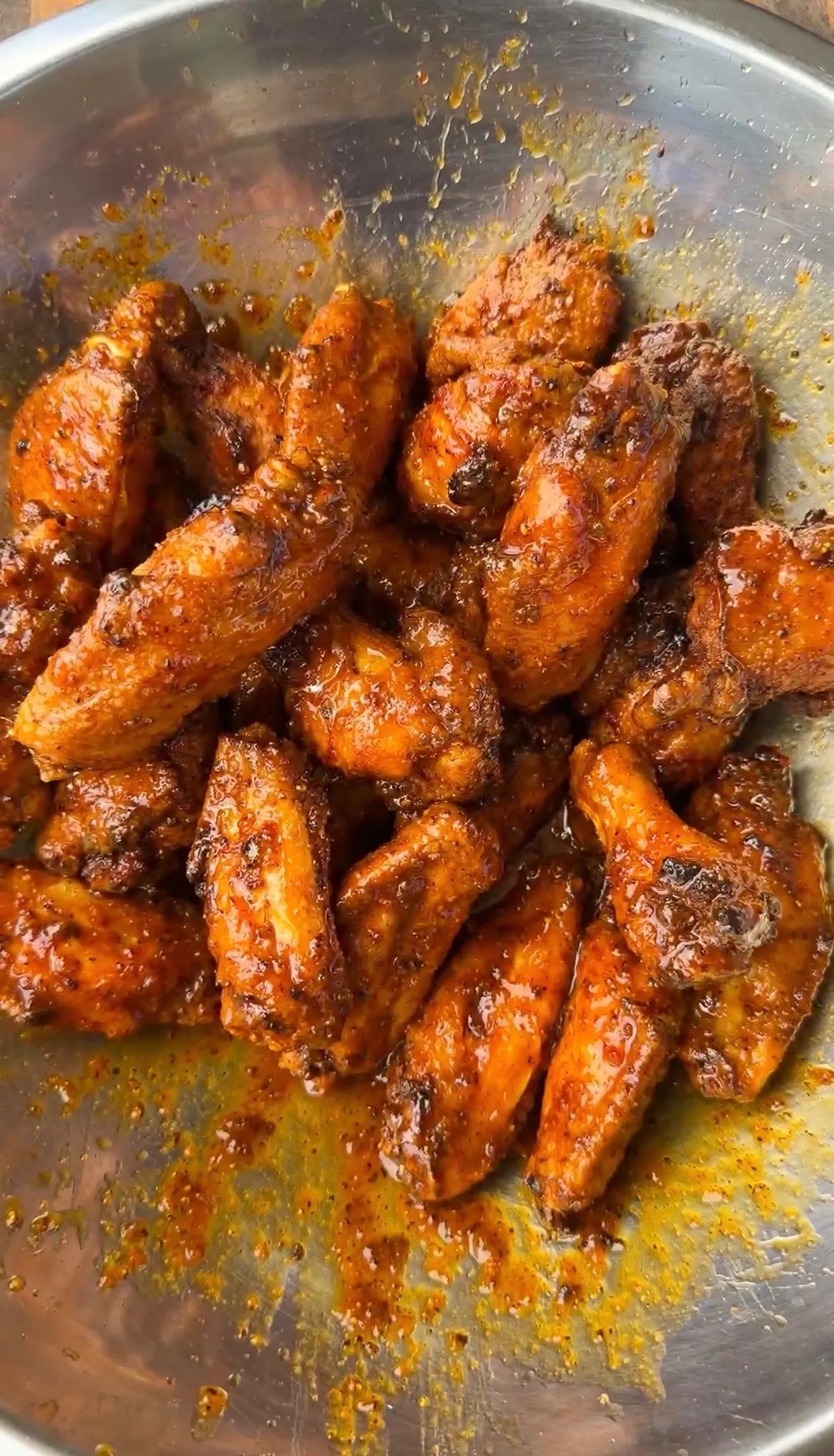 Glossy crispy fried honey lemon pepper chicken wings tossed in sauce in a stainless steel mixing bowl