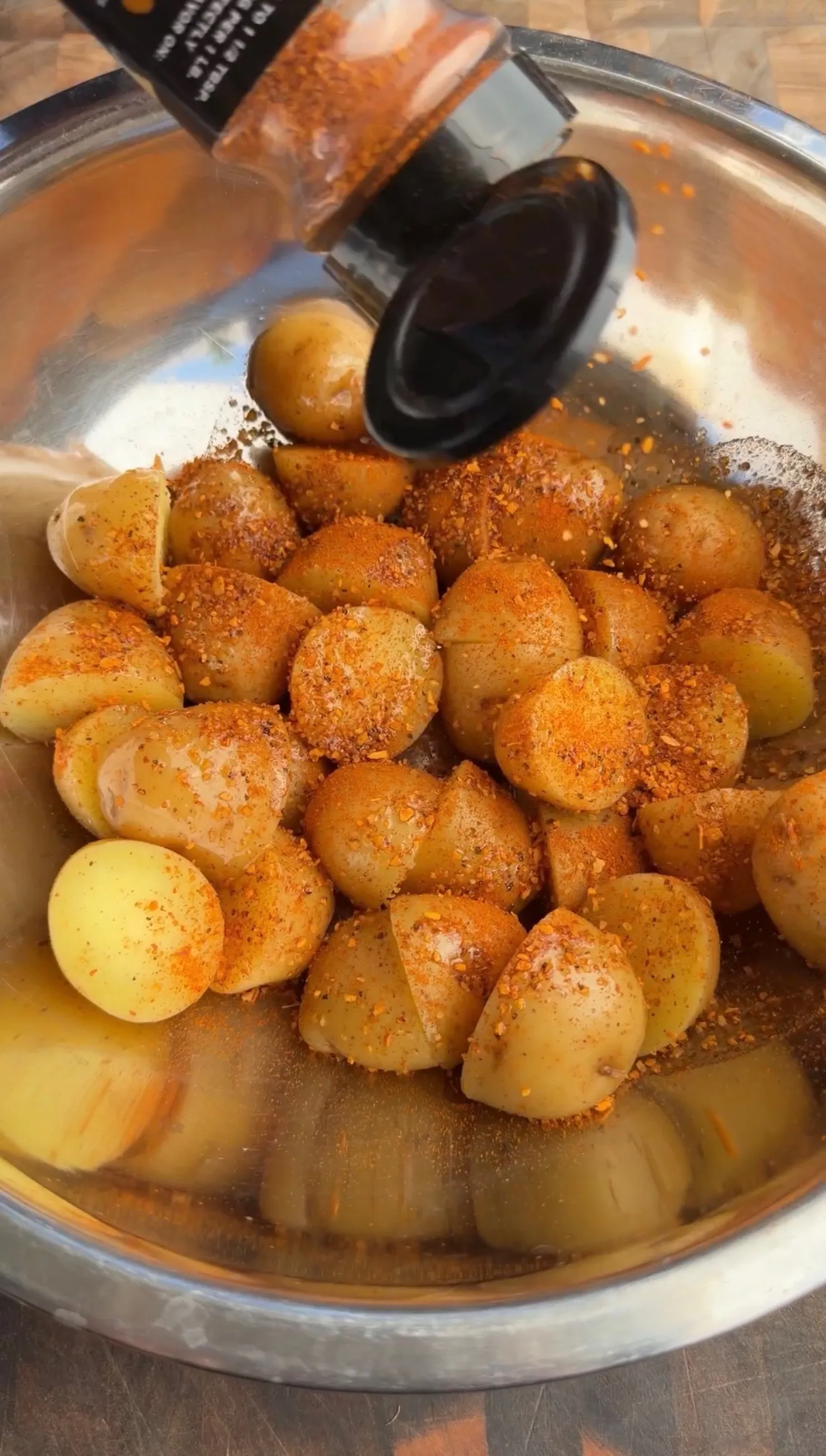 Golden crispy parmesan potatoes seasoned with paprika in a stainless steel mixing bowl with black serving spoon