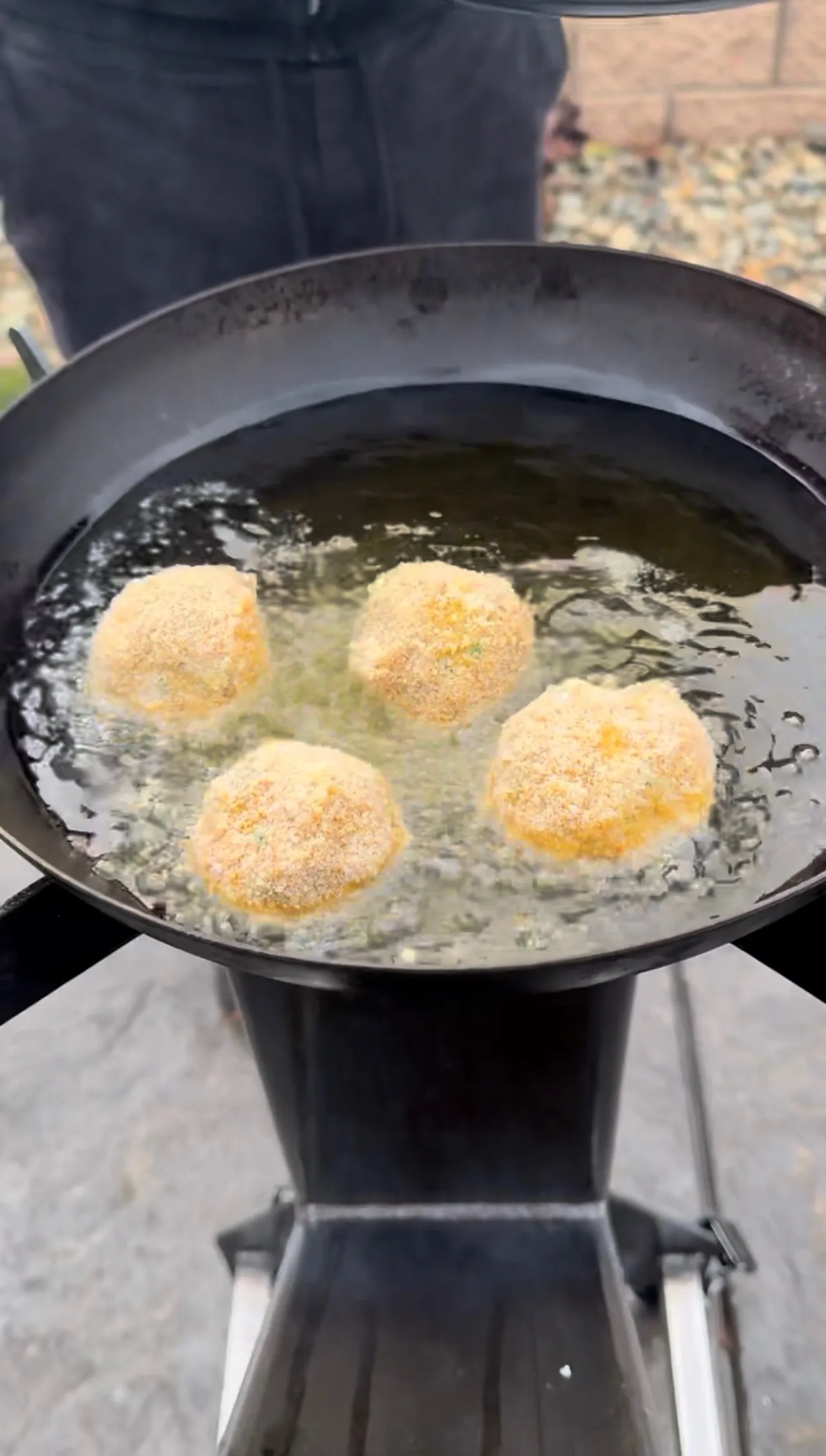 Four breaded jalapeño popper bites frying in hot oil in a large black cast iron skillet outdoors