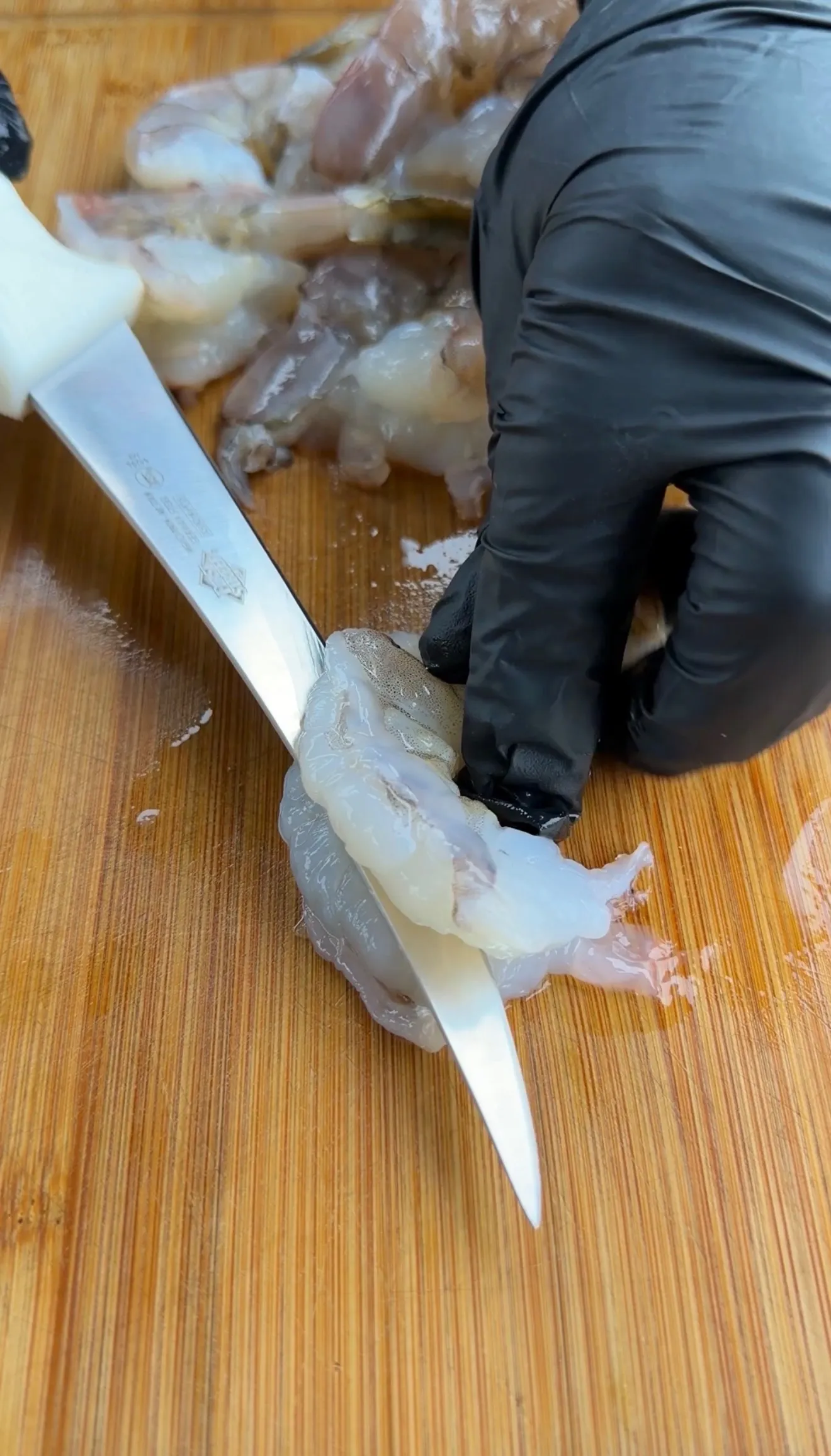 Gloved hand using a knife to clean and devein raw shrimp on a wooden cutting board for jalapeño popper stuffed shrimp