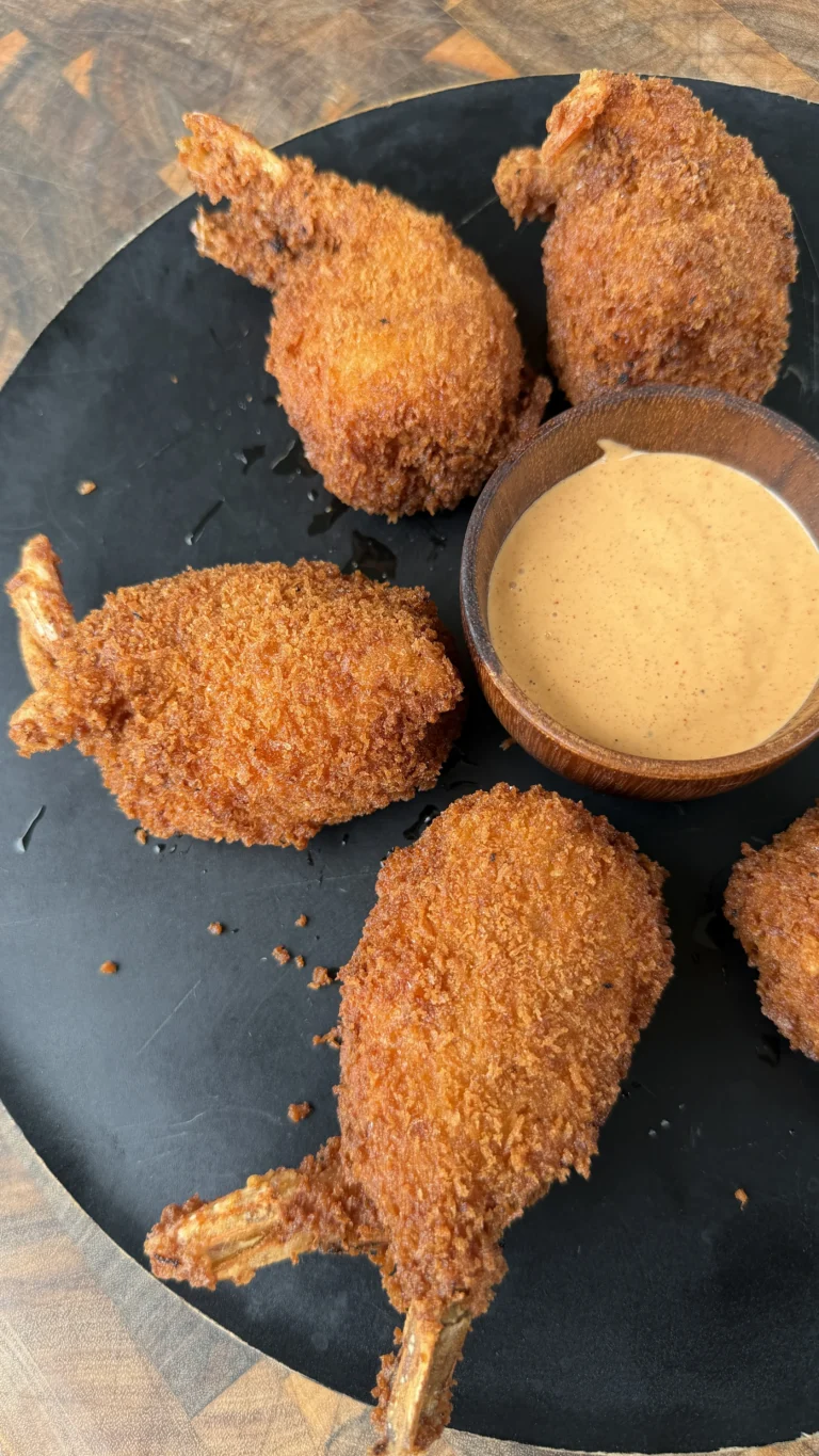 Golden crispy fried jalapeño popper stuffed shrimp on a black plate with creamy dipping sauce