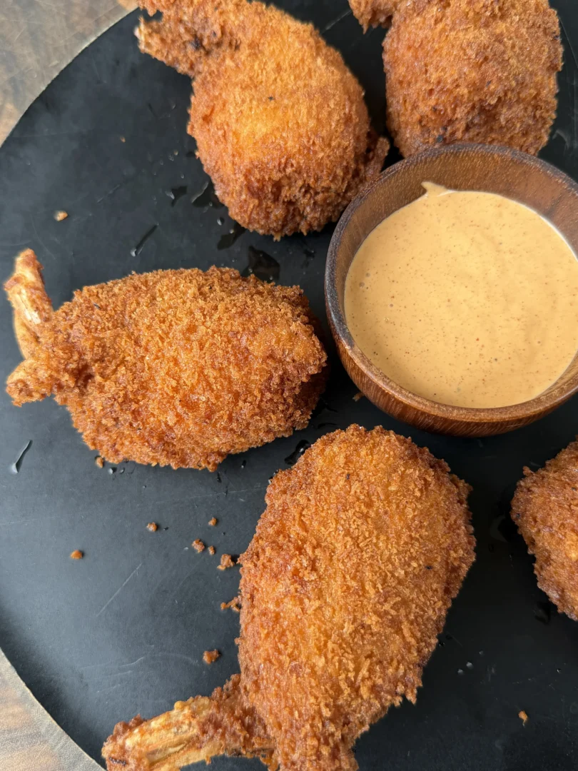 Golden crispy fried jalapeño popper stuffed shrimp on a black plate with creamy dipping sauce