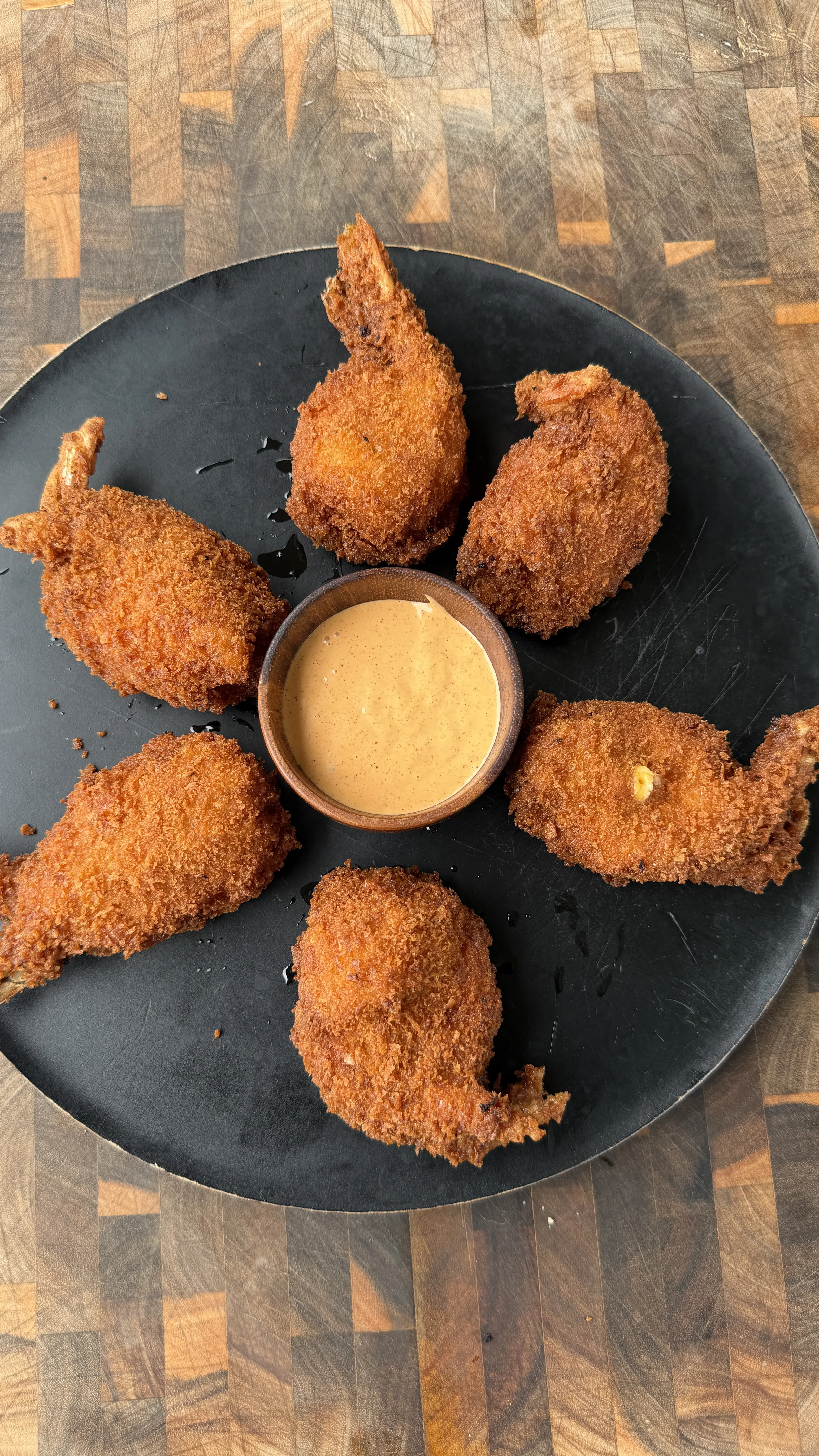 Golden fried jalapeño popper stuffed shrimp arranged on a dark plate with creamy dipping sauce in center