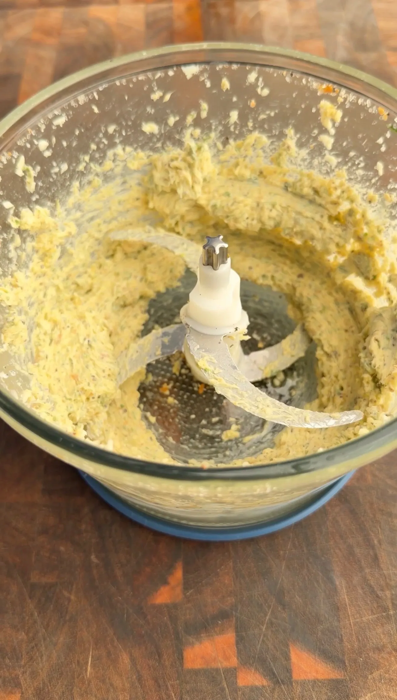 Creamy garlic herb butter mixture in a food processor bowl with blade attachment