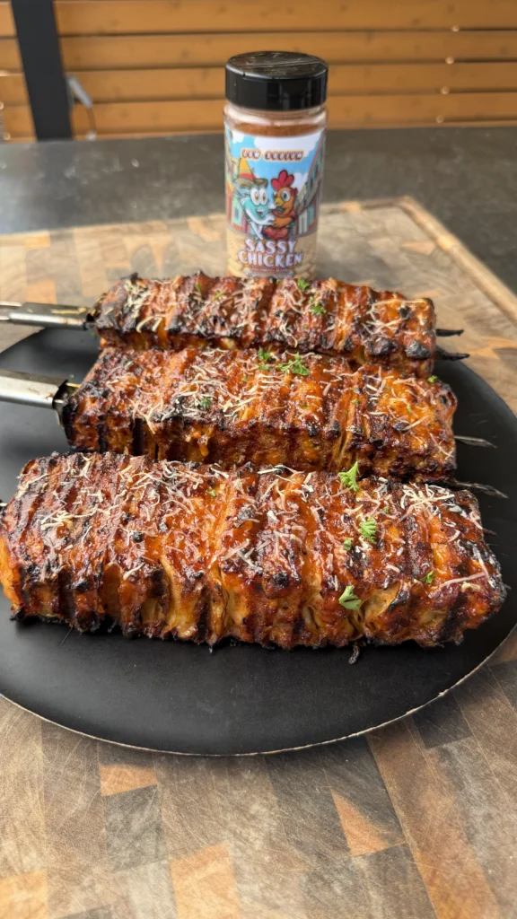 Three grilled buffalo chicken tortilla kebabs with melted cheese and herbs on a black plate with seasoning bottle