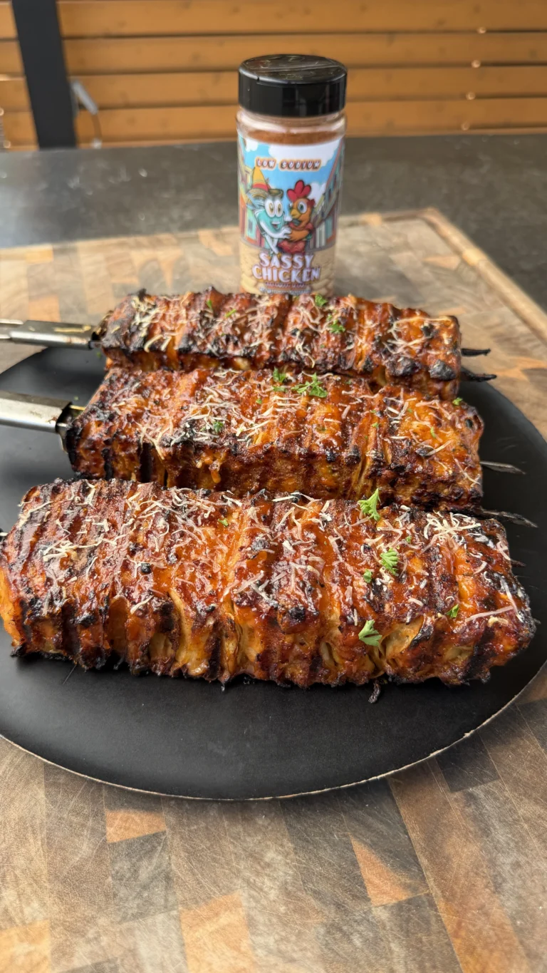 Three grilled buffalo chicken tortilla kebabs with melted cheese and herbs on a black plate with seasoning bottle