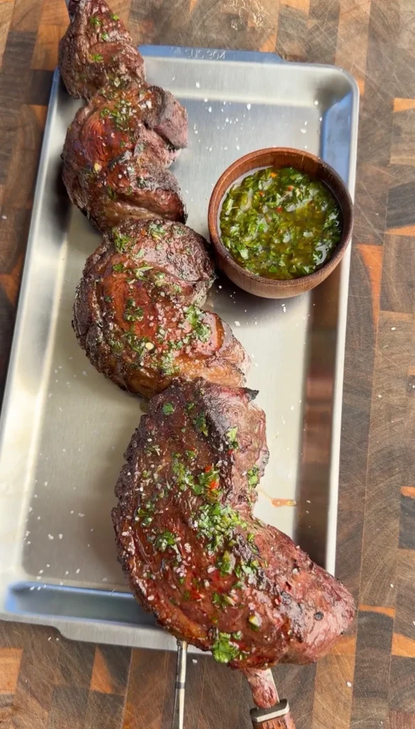 Grilled picanha beef skewer with charred jalapeño chimichurri sauce on white serving tray