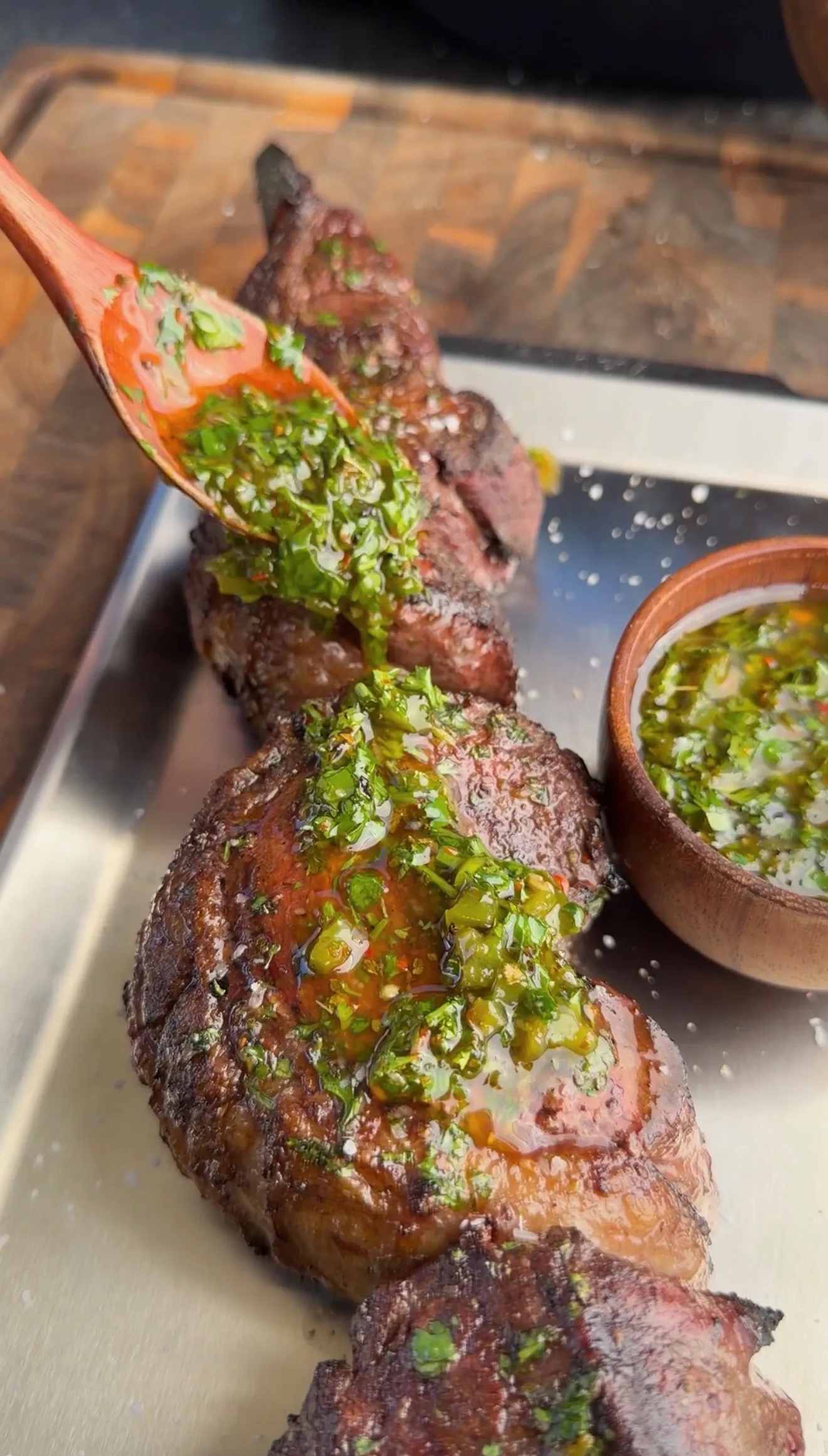 Grilled picanha steak topped with green jalapeño chimichurri sauce on a white platter with sauce bowl