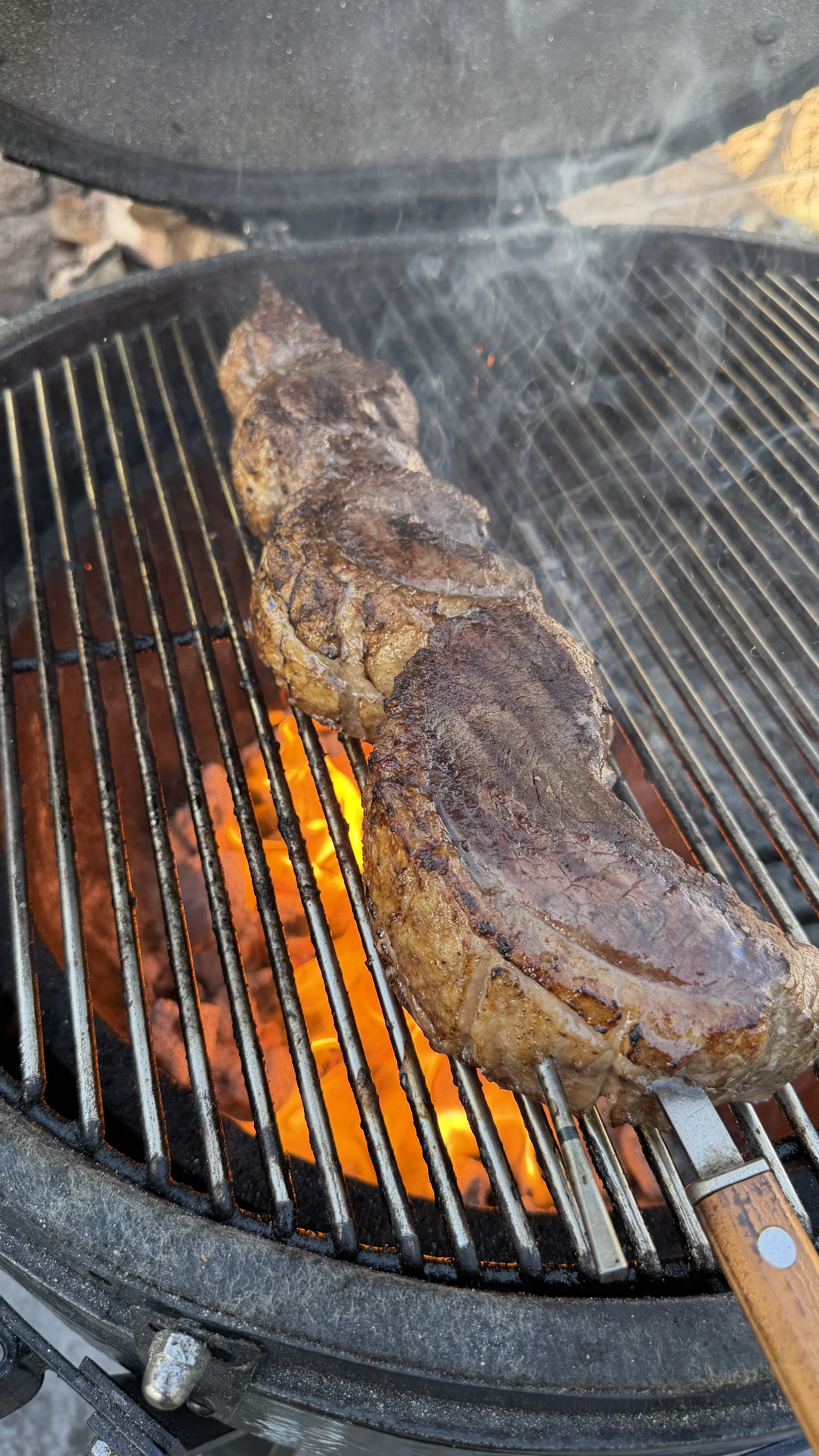 Picanha steak grilling over open flames on a round grill grate with visible char marks and smoke