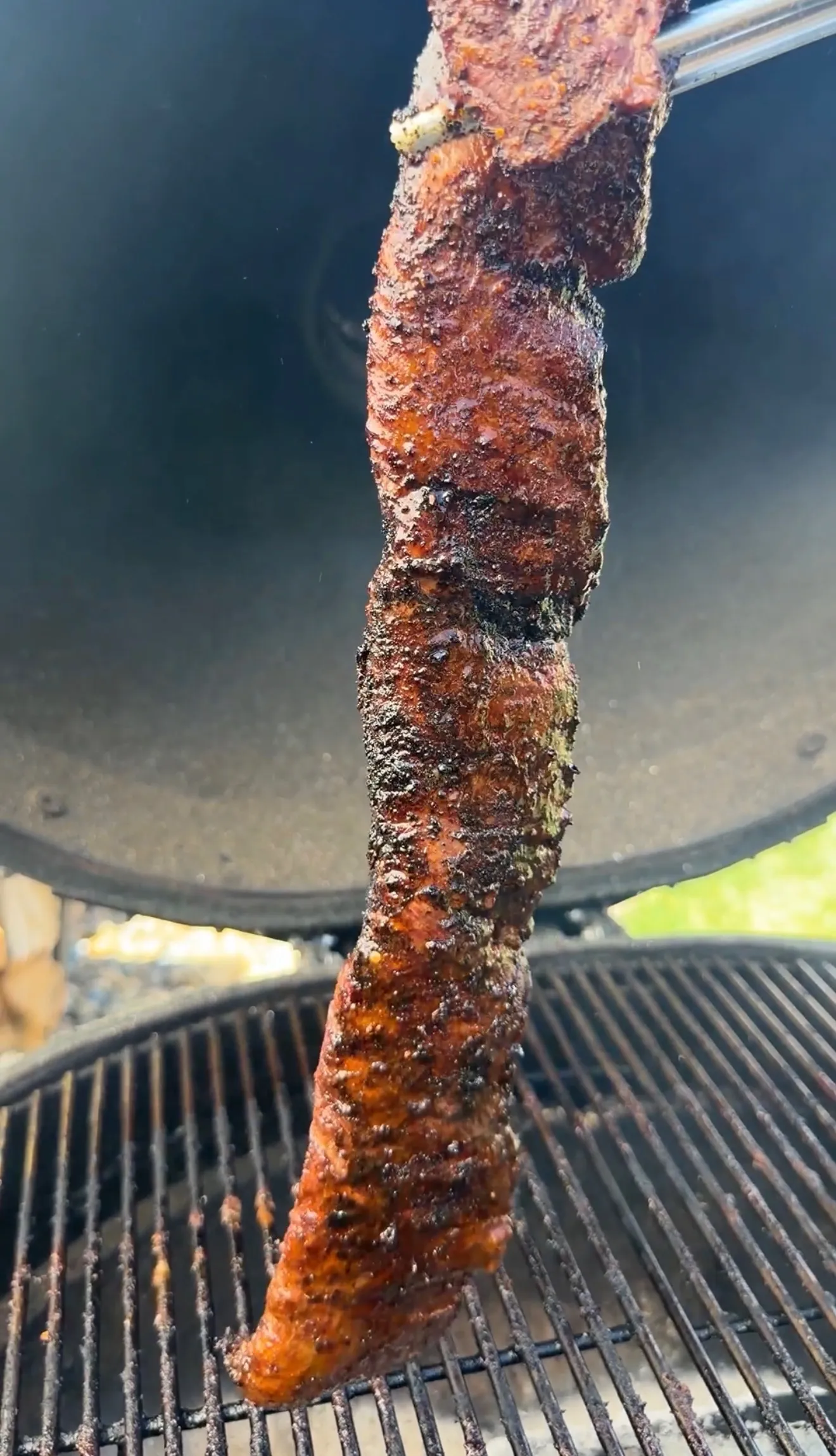 Charred skirt steak being grilled on barbecue grates with visible char marks and seasoning