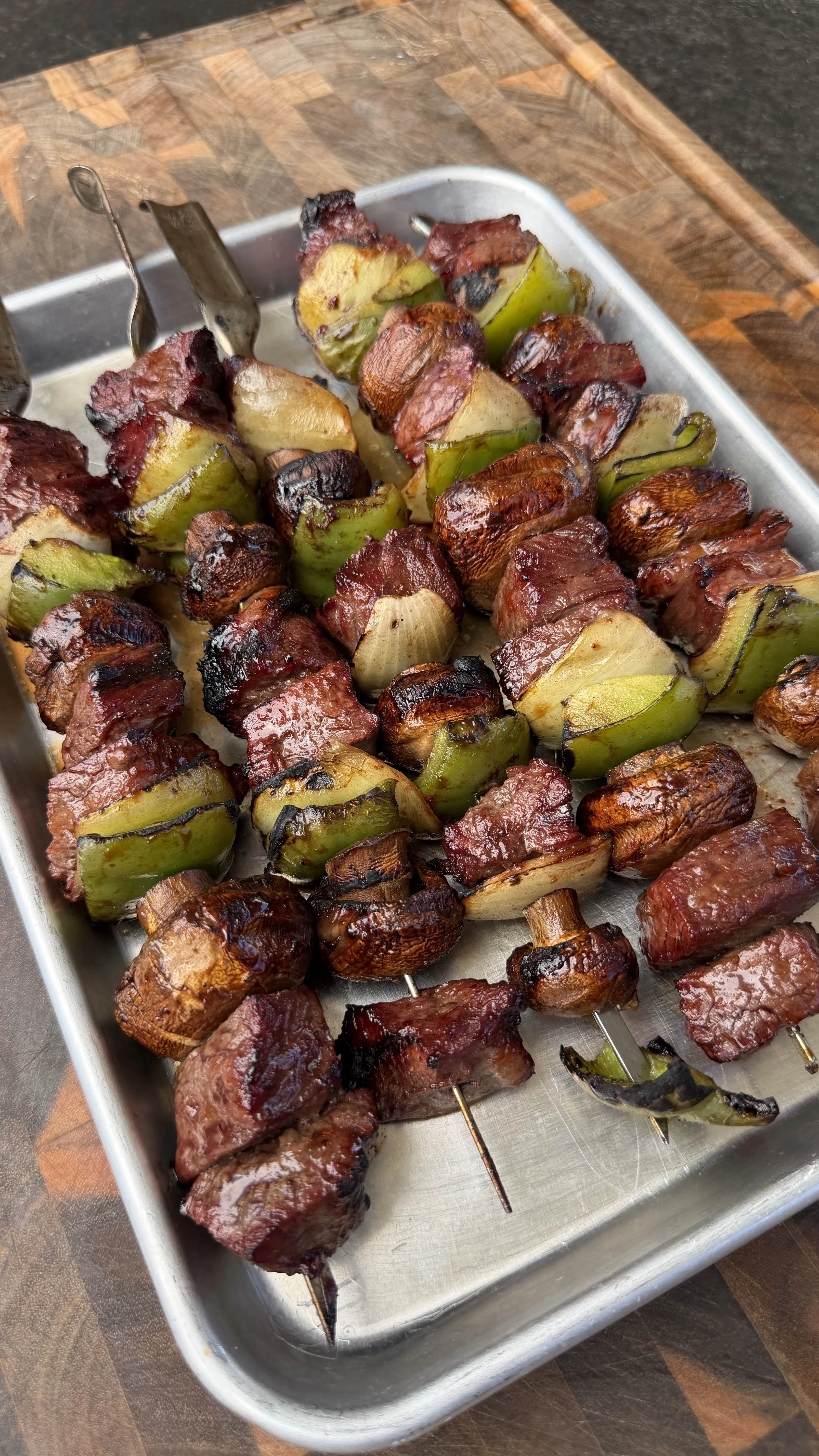Grilled teriyaki beef skewers with mushrooms and peppers on metal tray, showing caramelized glaze